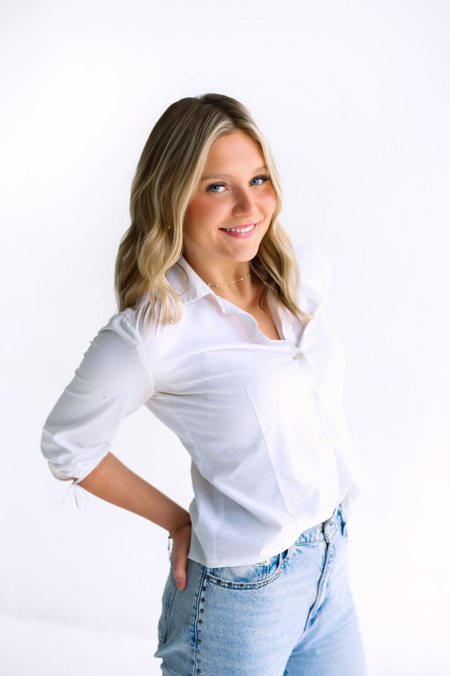 Studio portrait in classic white button-down shirt and light wash denim against white backdrop.