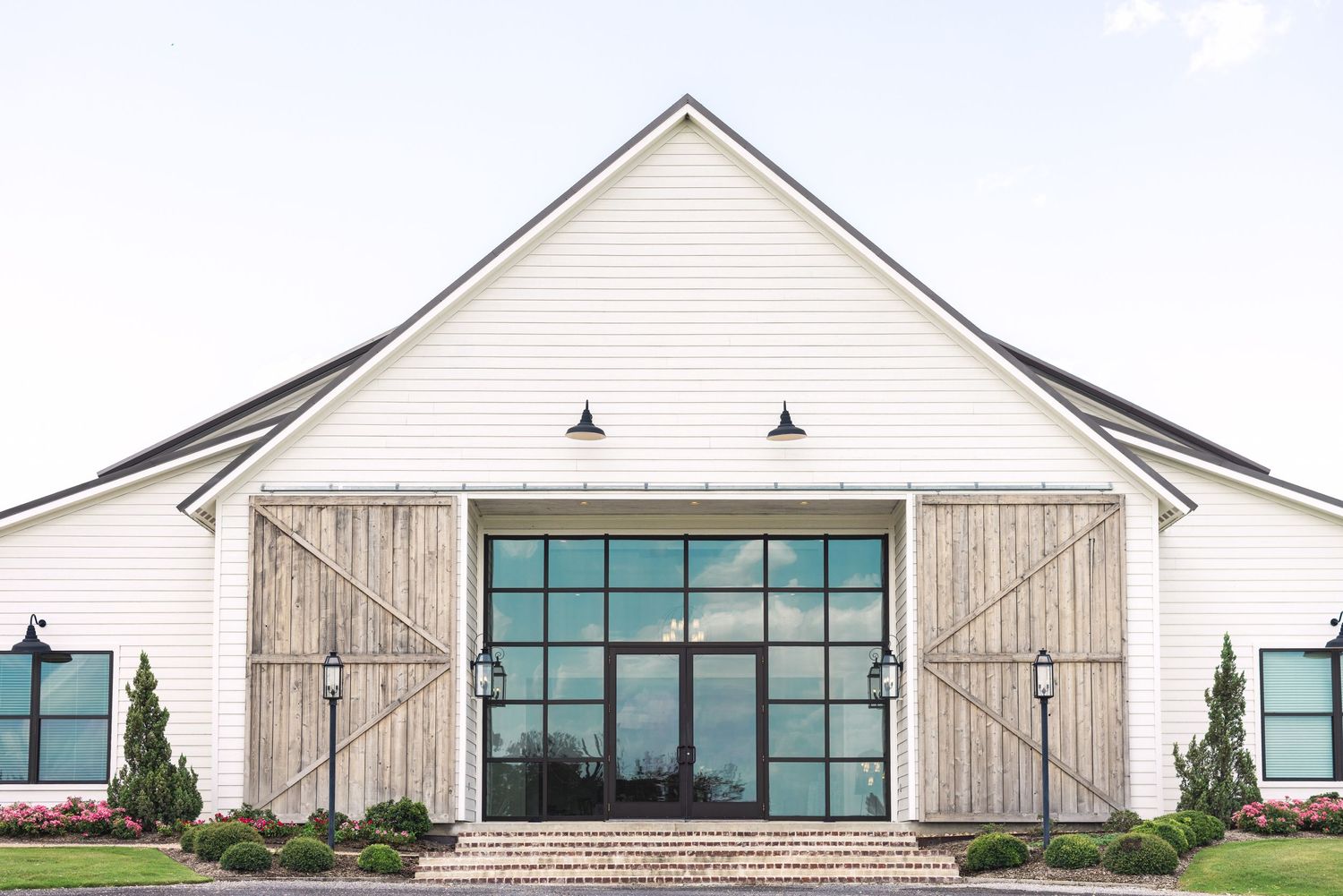 Modern white barn-style venue with large windows and rustic sliding doors.