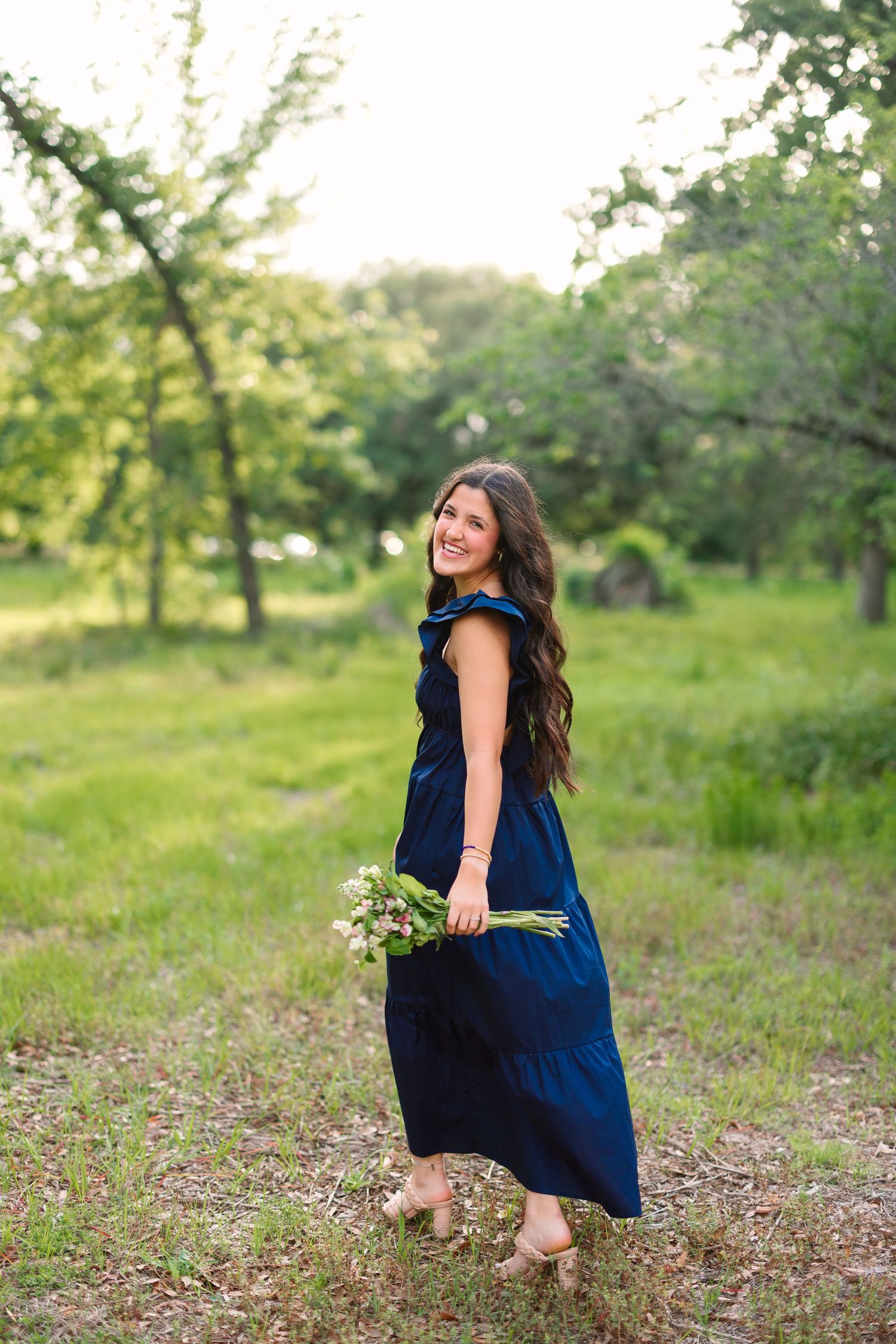 A person in a navy blue dress poses playfully in a grassy field during golden hour.