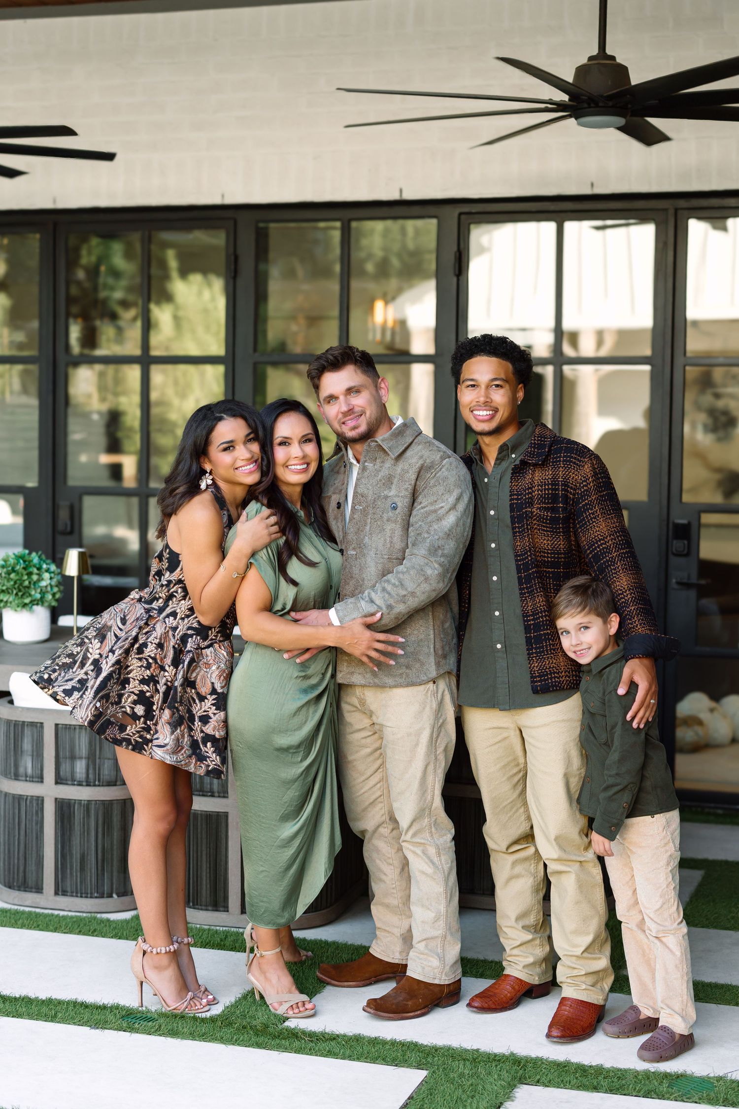 A joyful family of five poses together on a modern patio, wearing coordinated earth-tone outfits.
