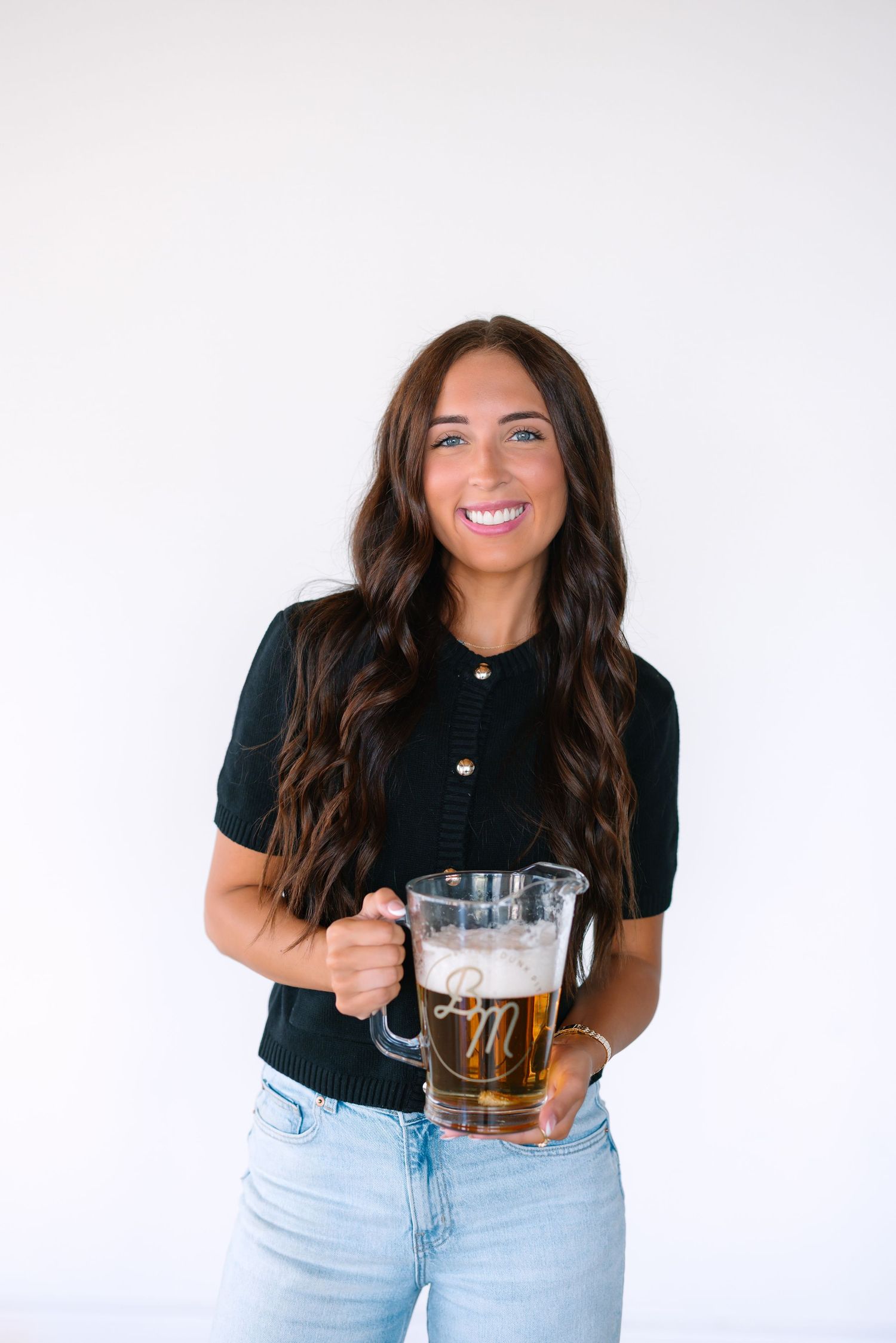 Person in black shirt and jeans holding a glass mug against white background.