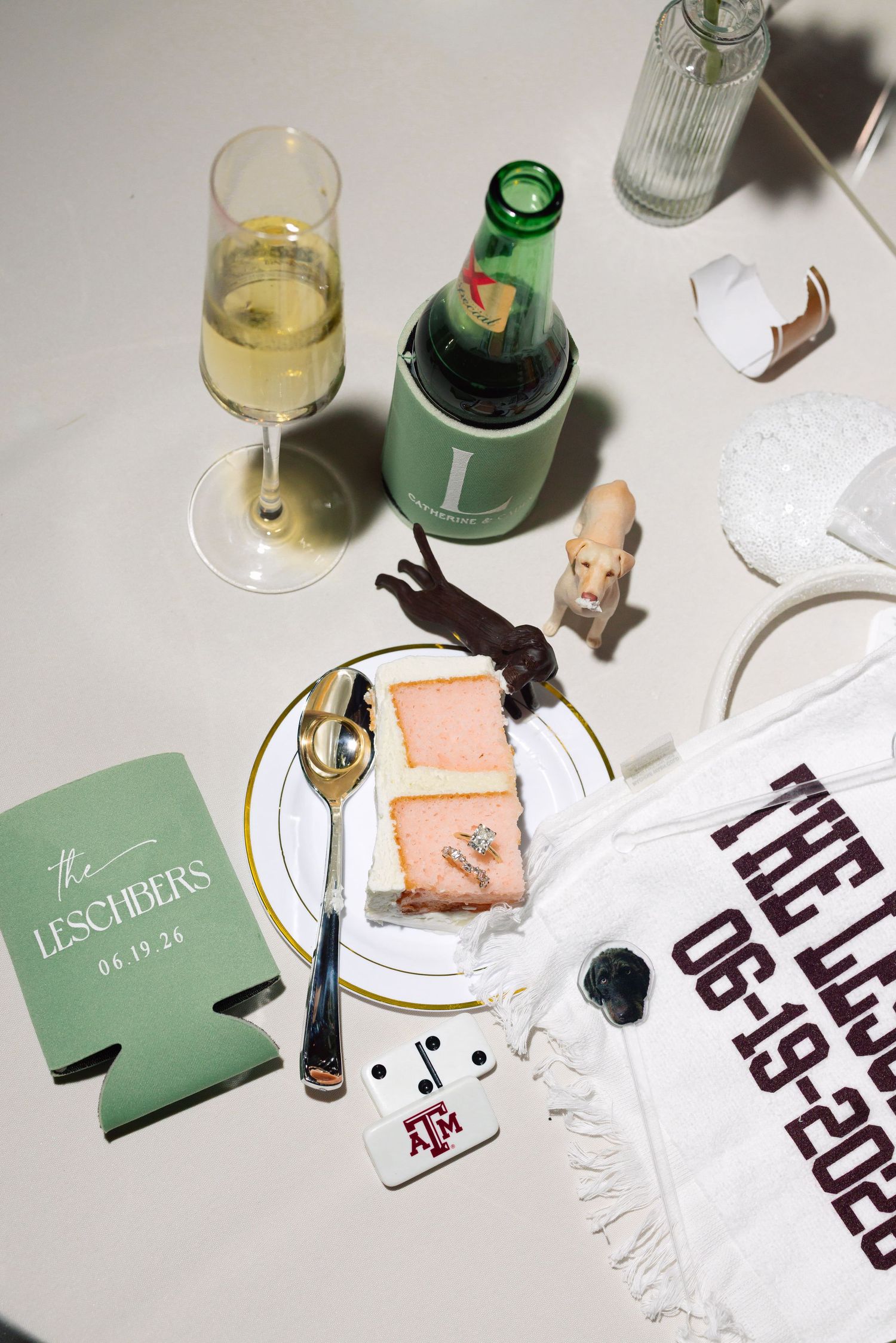 Wedding flat lay featuring champagne, cake, Texas A&M koozies, and personalized Lescher wedding memorabilia.