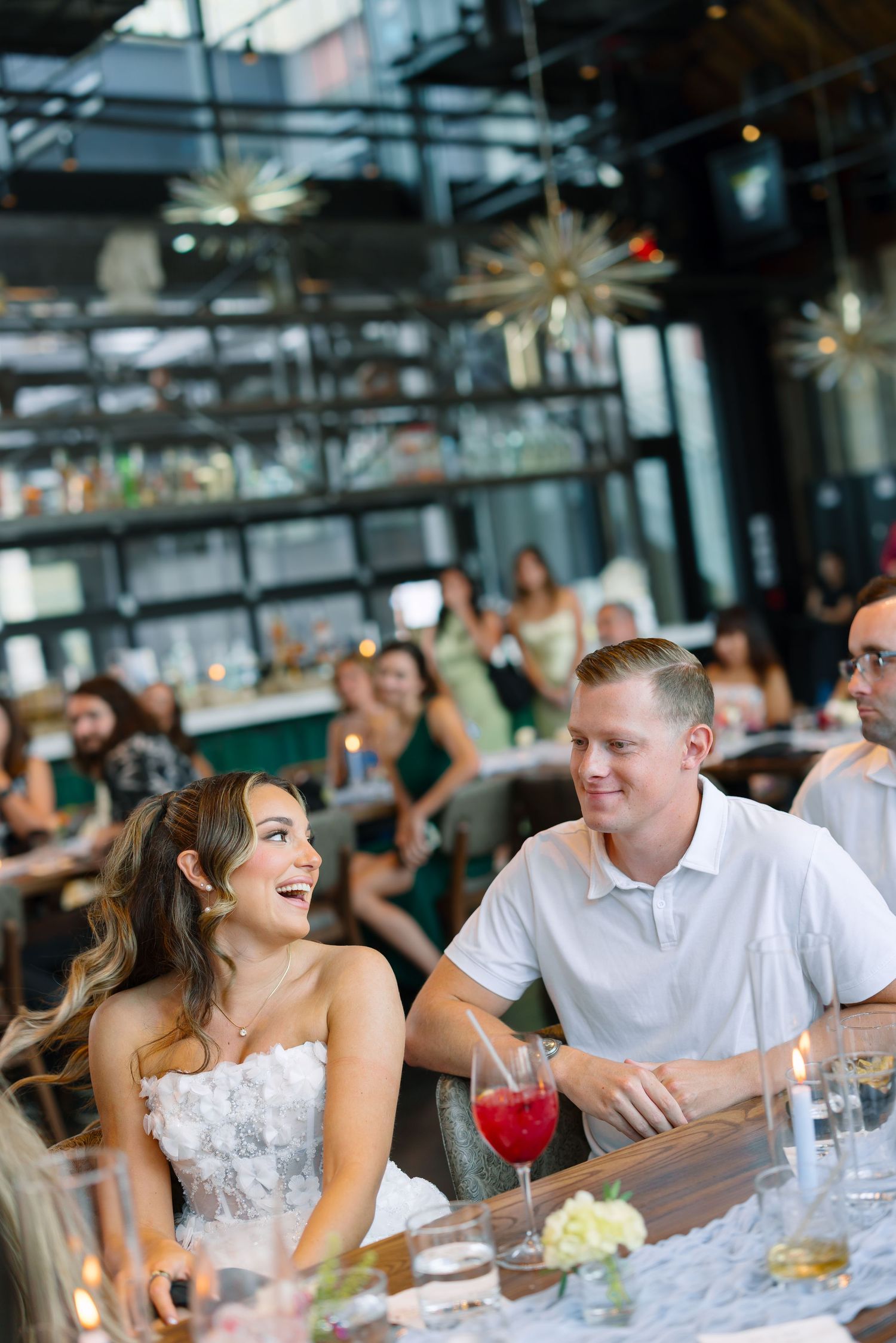 Bride in white strapless gown laughing with guests at elegant wedding reception dinner with gold star pendant lights.