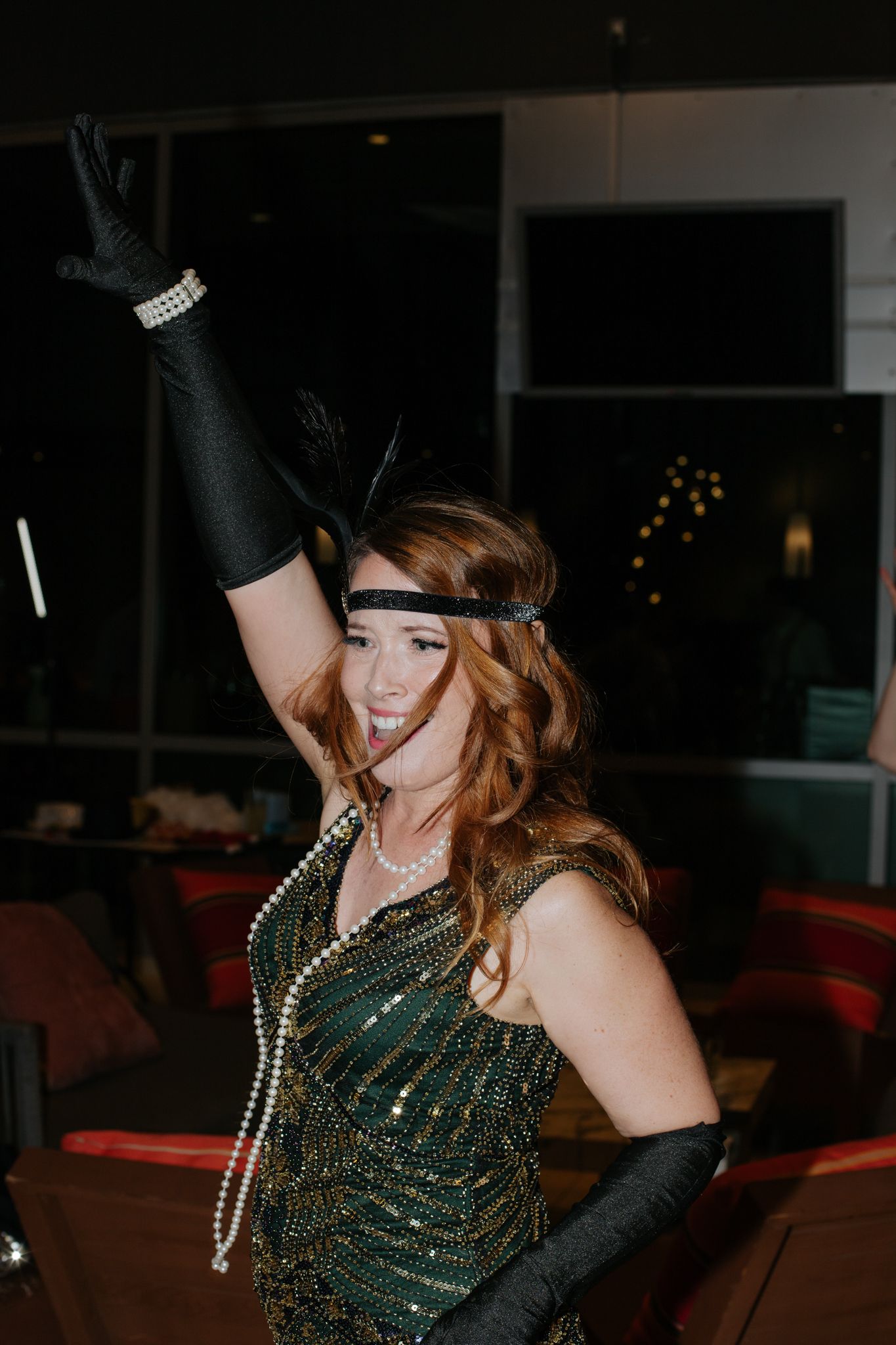 A person wearing a sparkling green dress with black gloves poses dramatically in a dark room.
