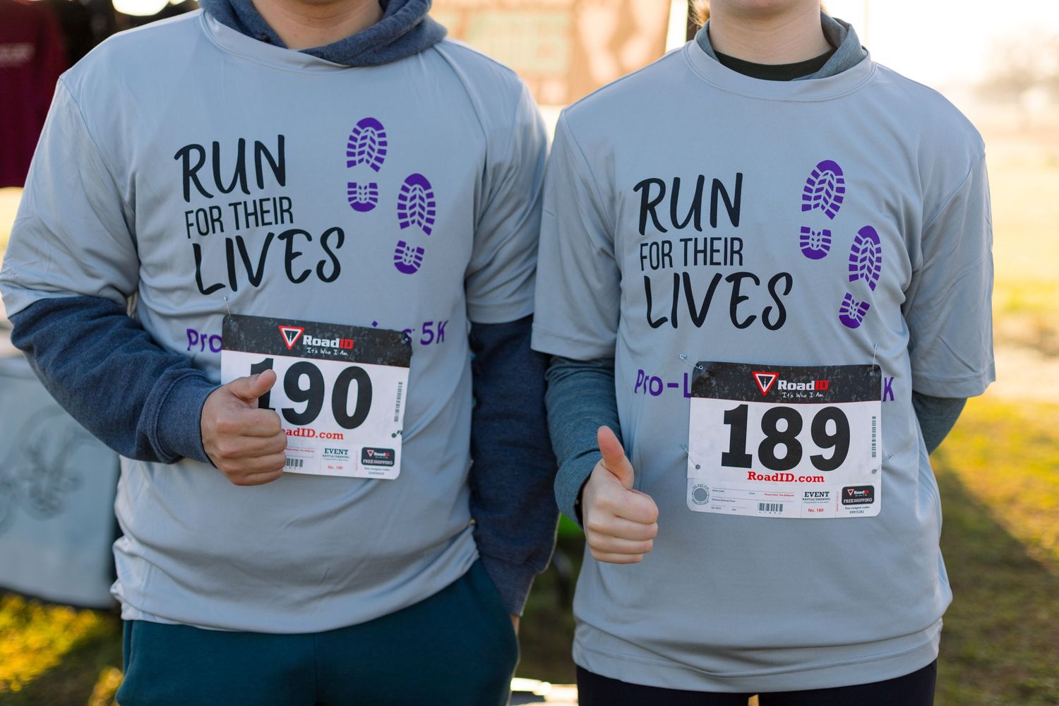 Runners wearing race bibs and gray sweatshirts at charity run event.