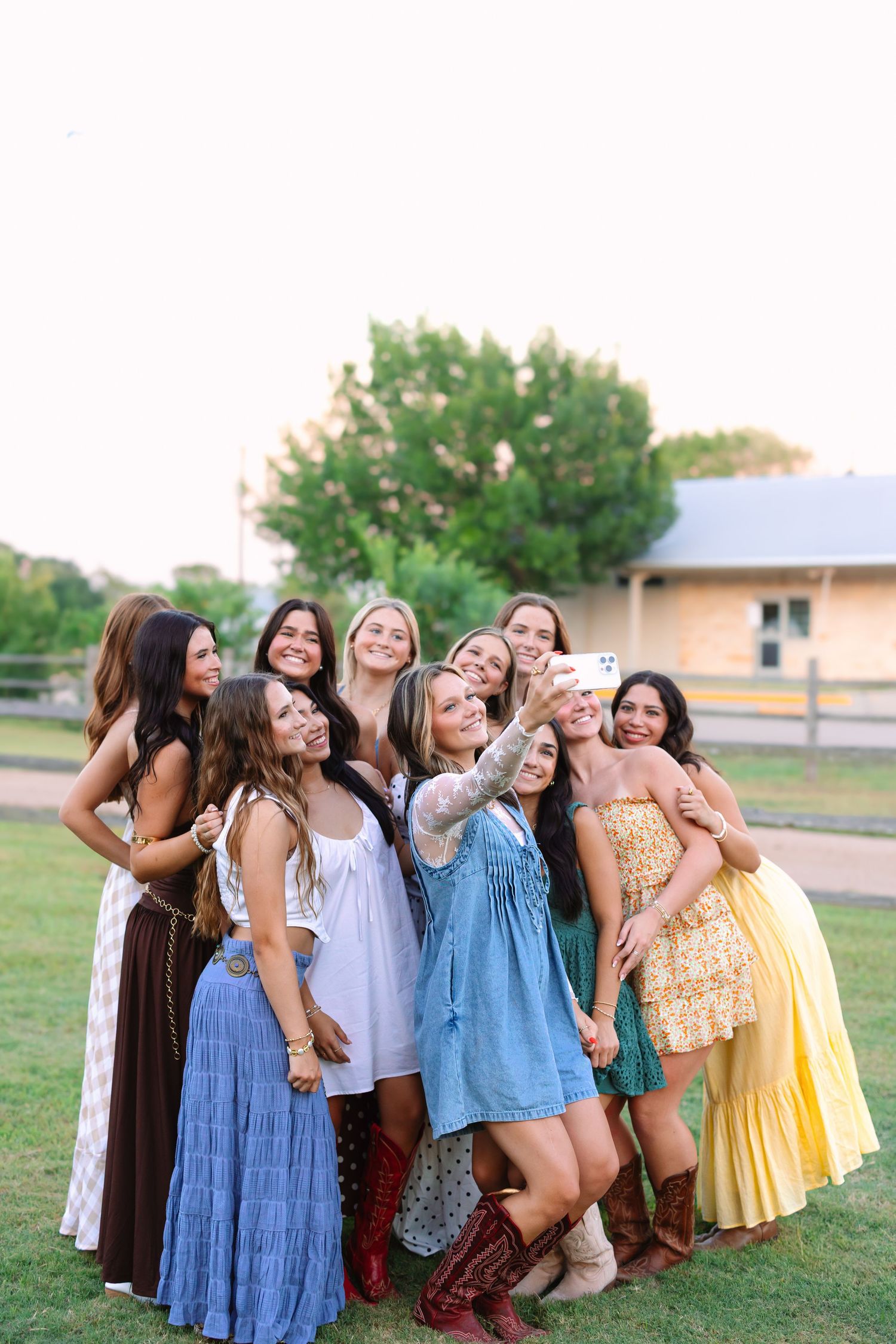Friends in sundresses laugh together while posing for group photos on a grassy hill.