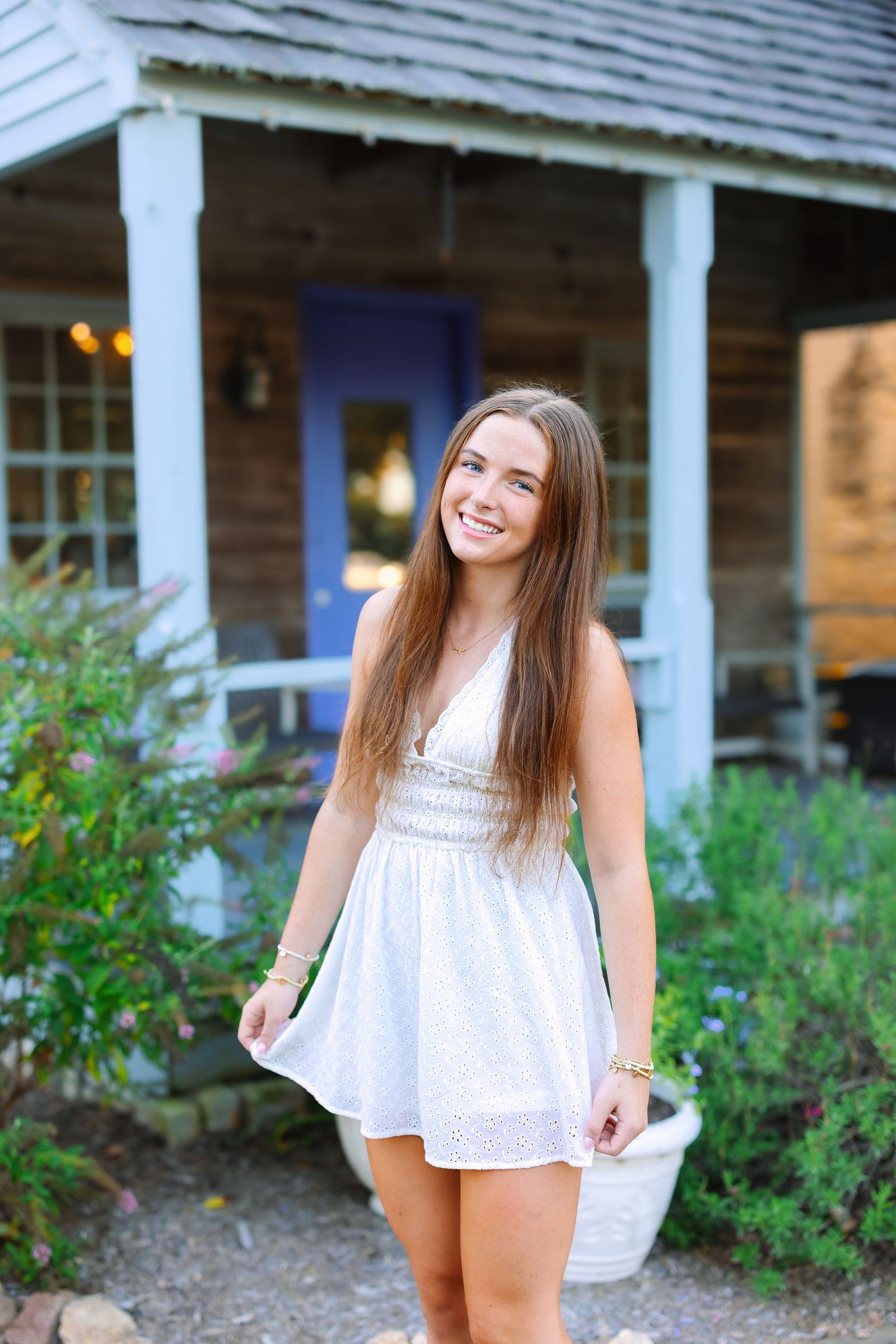 A white eyelet dress is showcased against a rustic porch with blooming garden flowers.