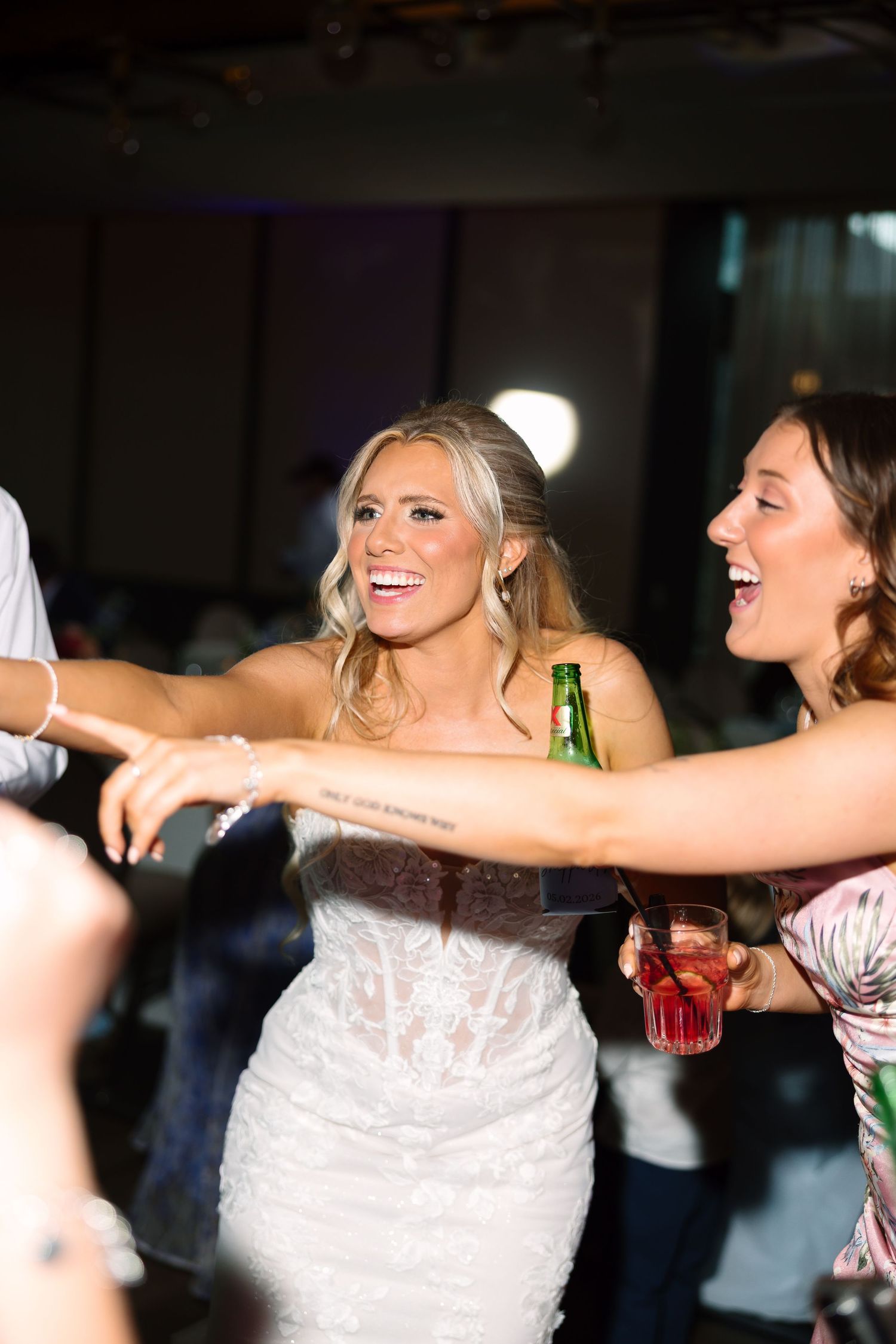 Smiling bride in lace gown dancing joyfully with guests at wedding reception.