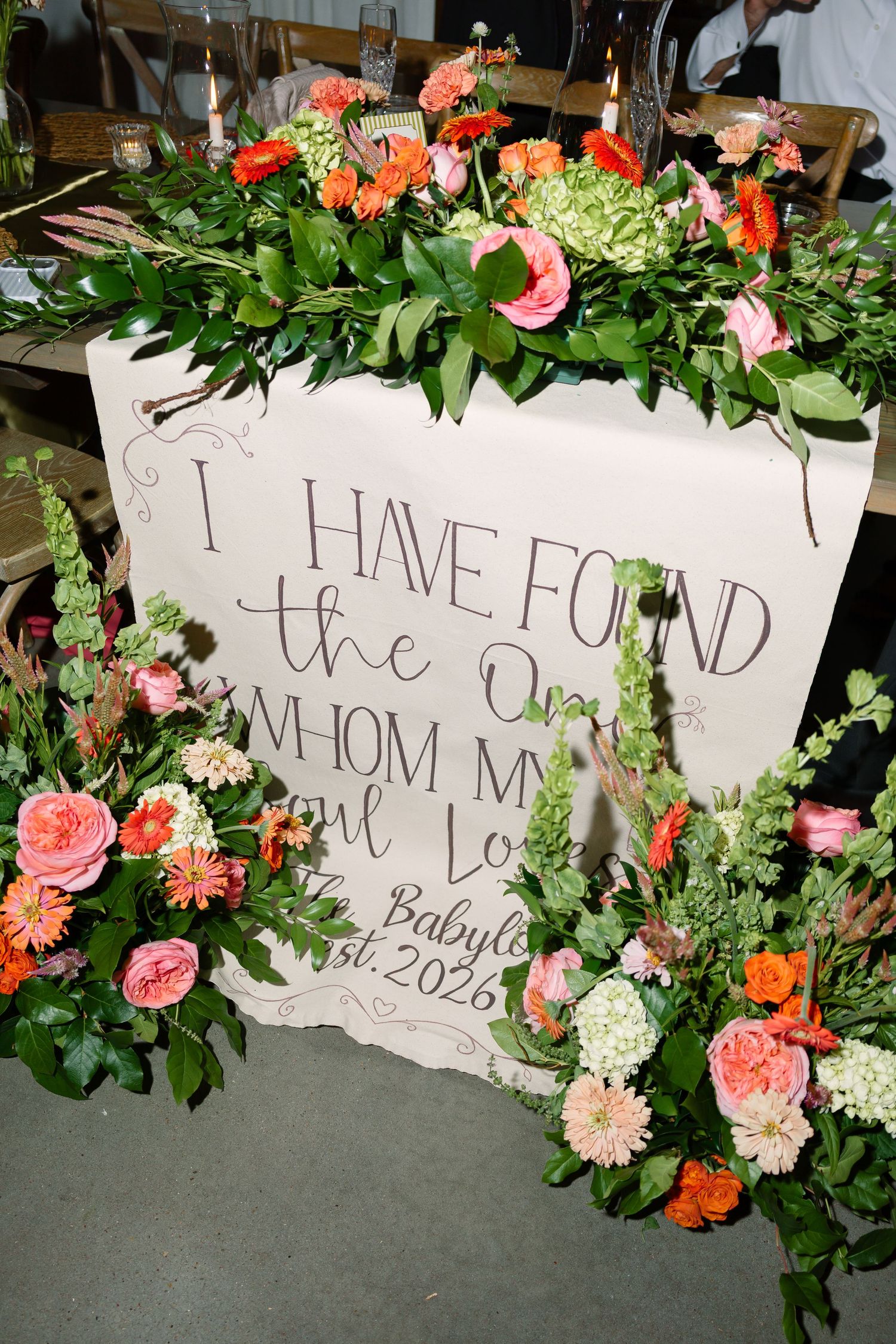 Wedding sign reading I Have Found the One Whom My Soul Loves surrounded by lush pink, coral, and green floral arrangements.