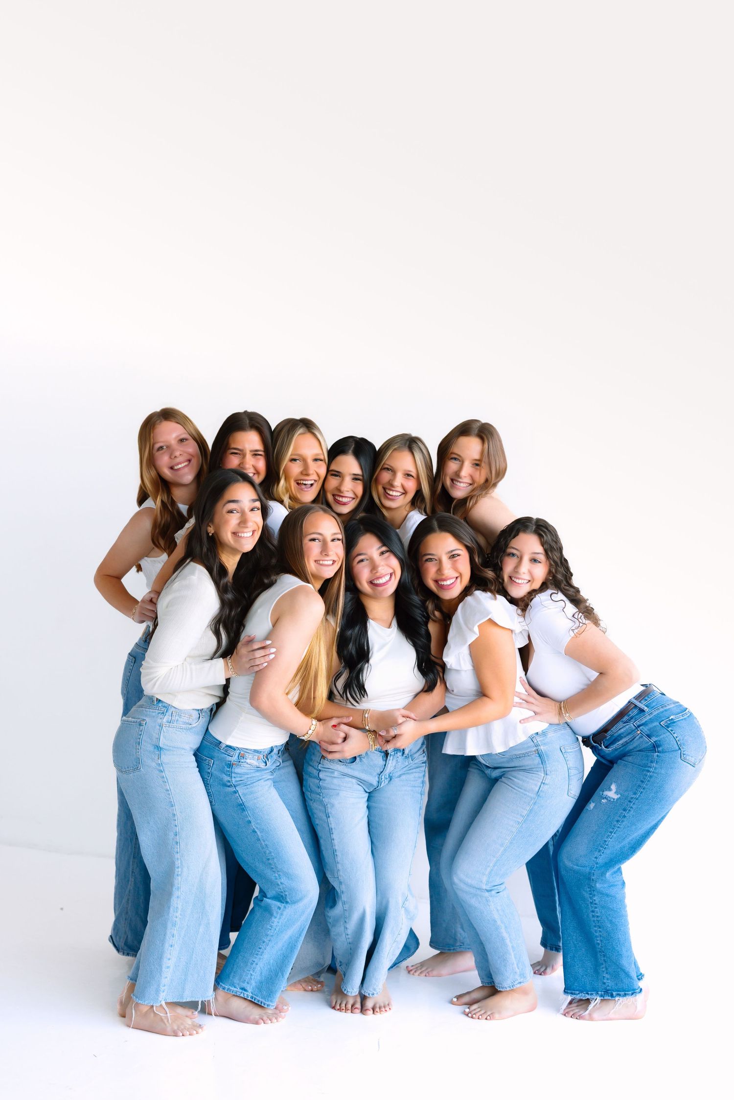 Cheerful group in matching white tops and jeans posing playfully against white background.