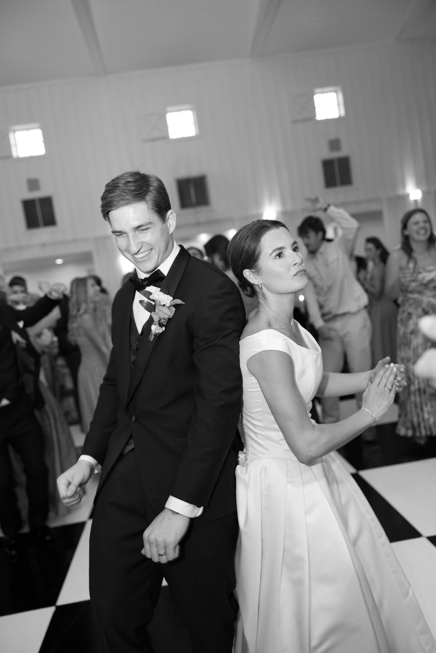Black and white photo of bride and groom dancing back-to-back on checkered dance floor at wedding reception.