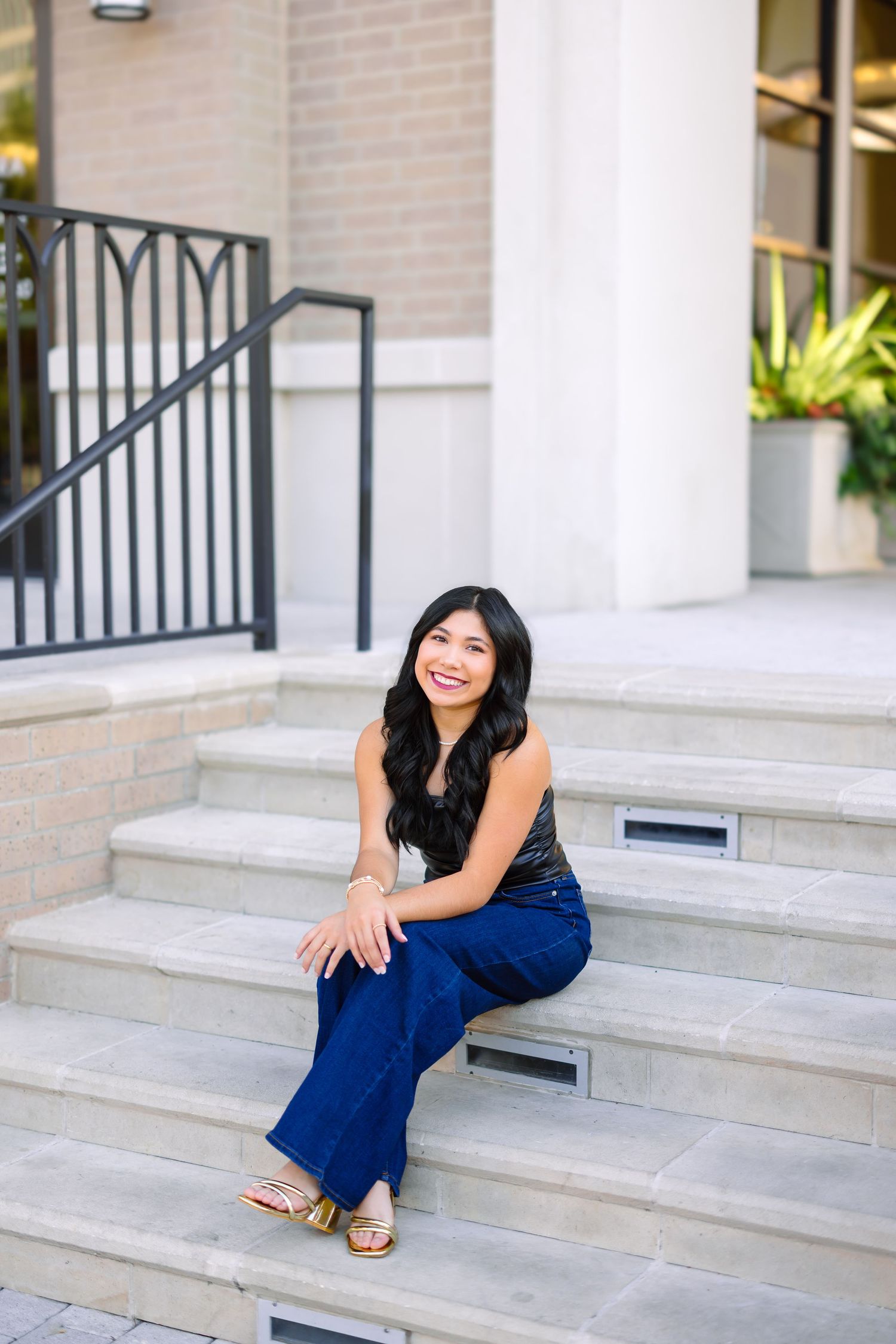 Woman in navy outfit sits smiling on concrete steps outside building.