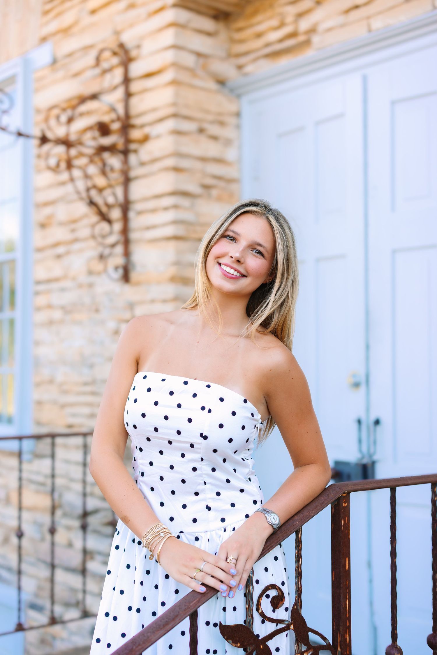 A polka dot dress is showcased against a rustic stone wall and white door backdrop.