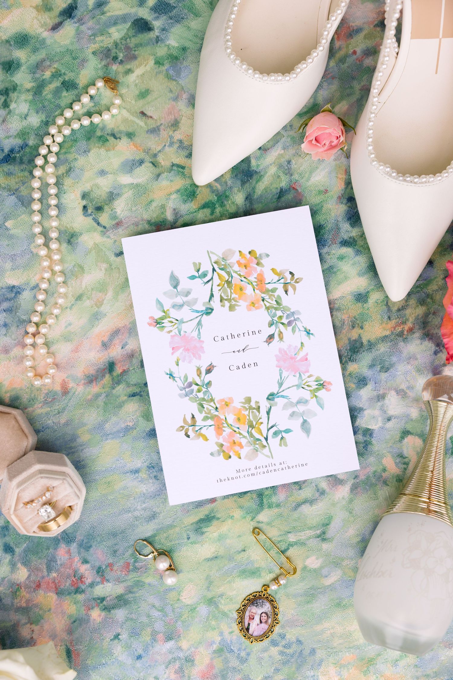 Elegant wedding flat lay with floral invitation, pearl necklace, white heels, and bridal accessories on a soft green background.