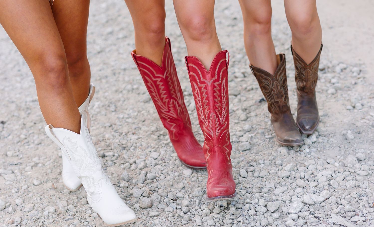 Brown leather cowboy boots and white sneakers shown walking on concrete ground.