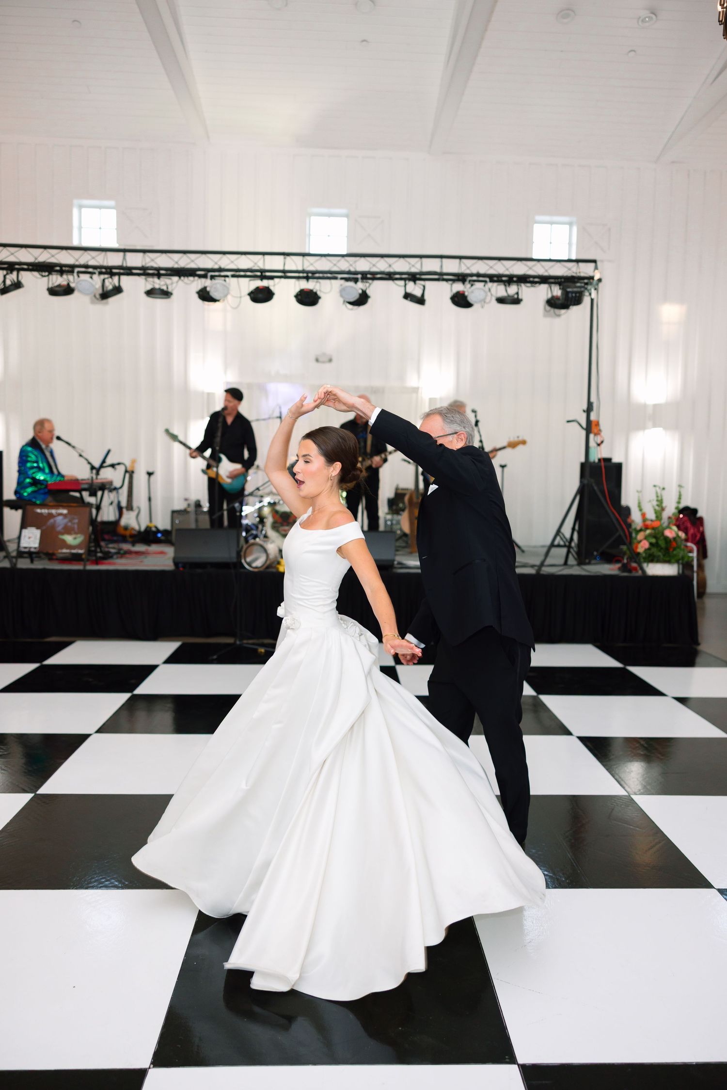 Bride and groom share first dance on black and white checkered floor with live band performing behind them.
