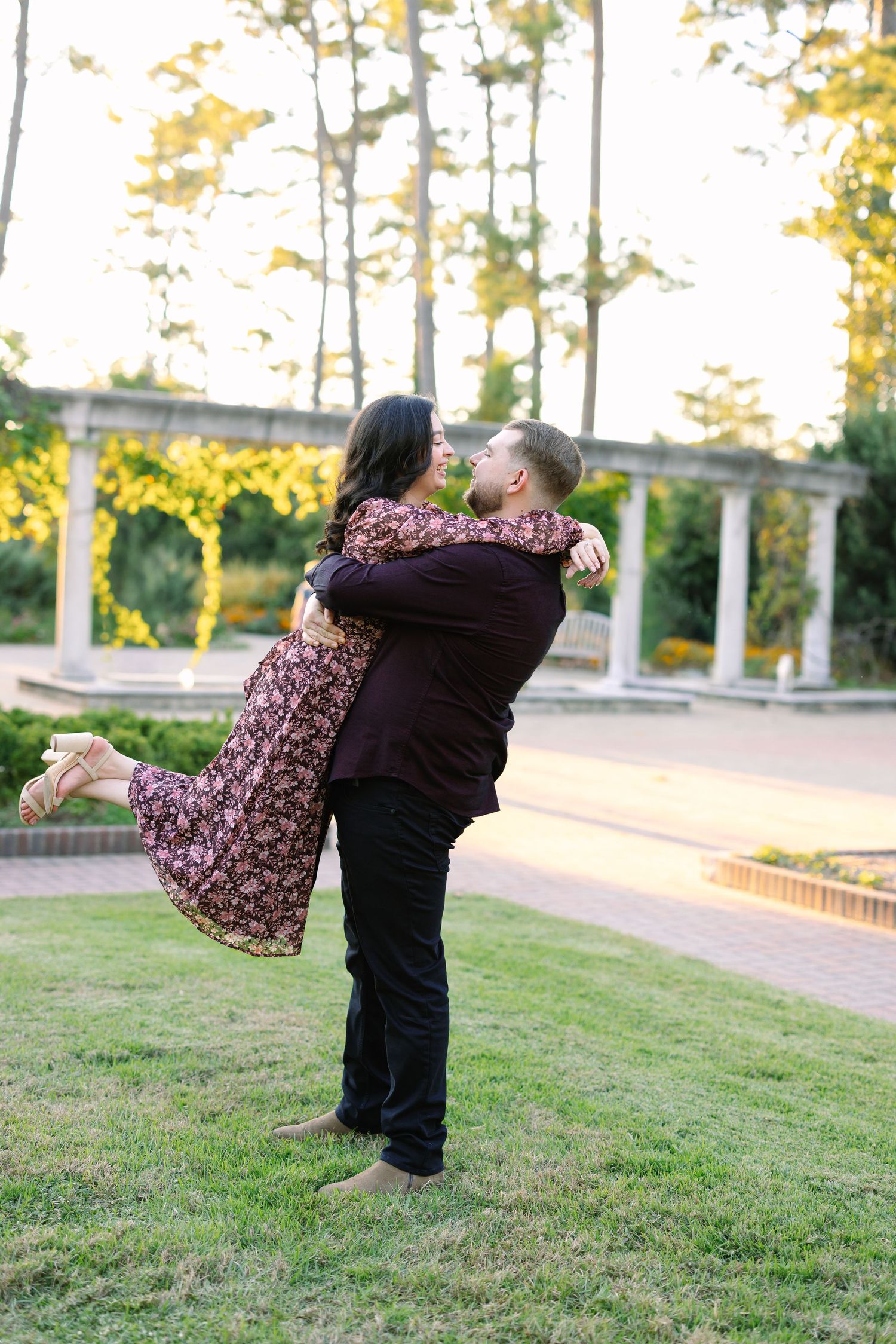 Playful couple dancing and twirling on grass during sunset photo session.