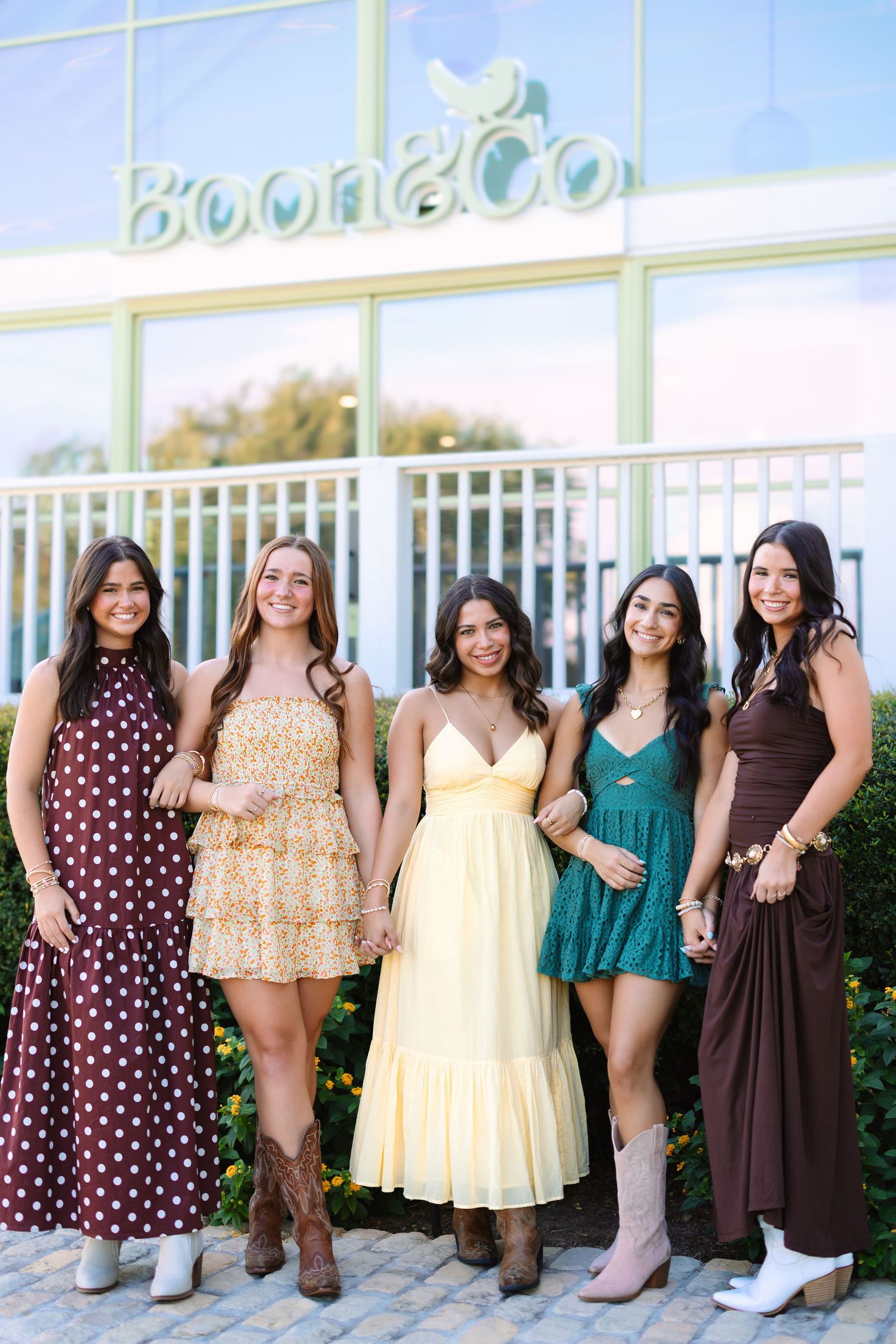 A group in summer dresses poses together against a storefront window.