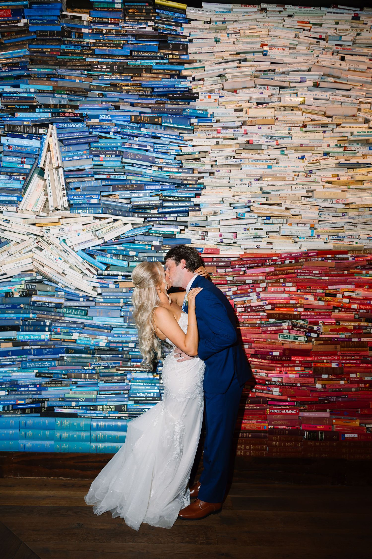 Newlyweds share first kiss in front of a colorful Texas flag made entirely of stacked books.