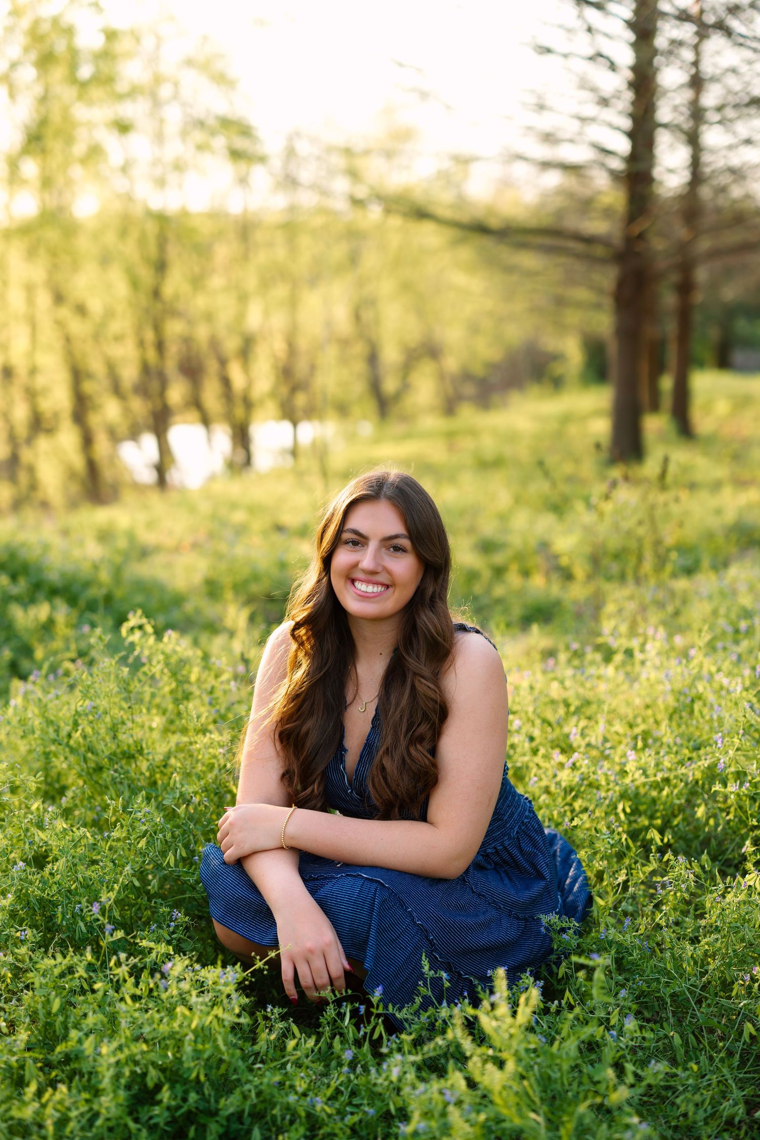 Graduate in navy dress poses in field of wildflowers during sunset.
