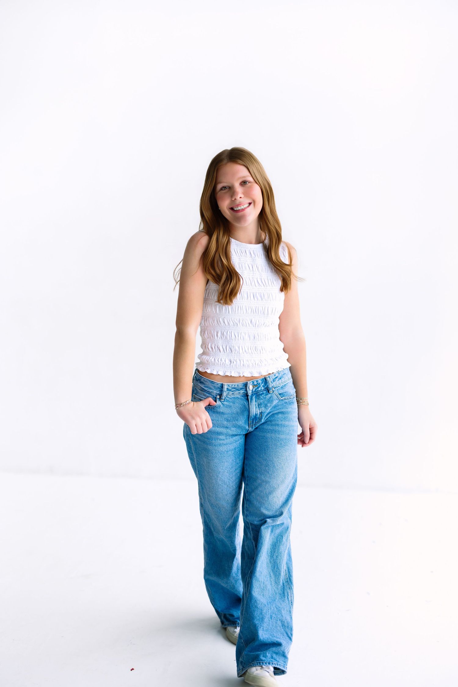 Full length portrait in white smocked top and wide leg jeans against white background.