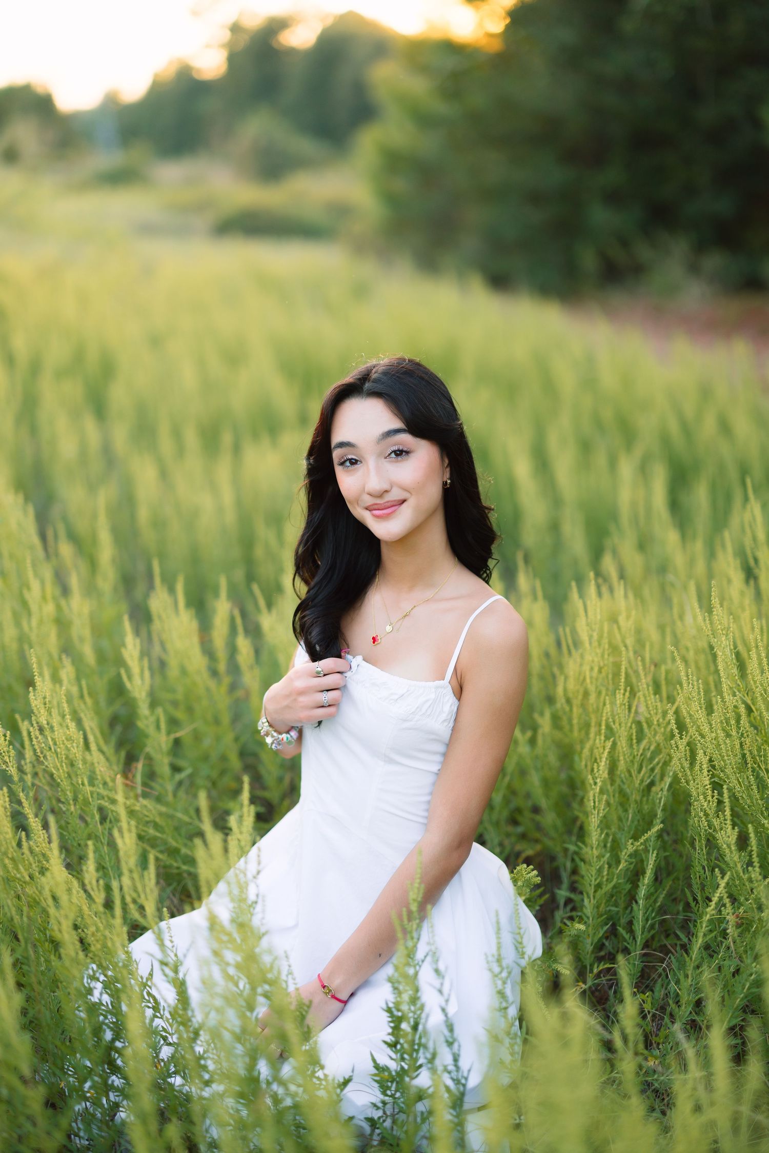 Summer portraits in a white dress amid tall green grass at sunset.