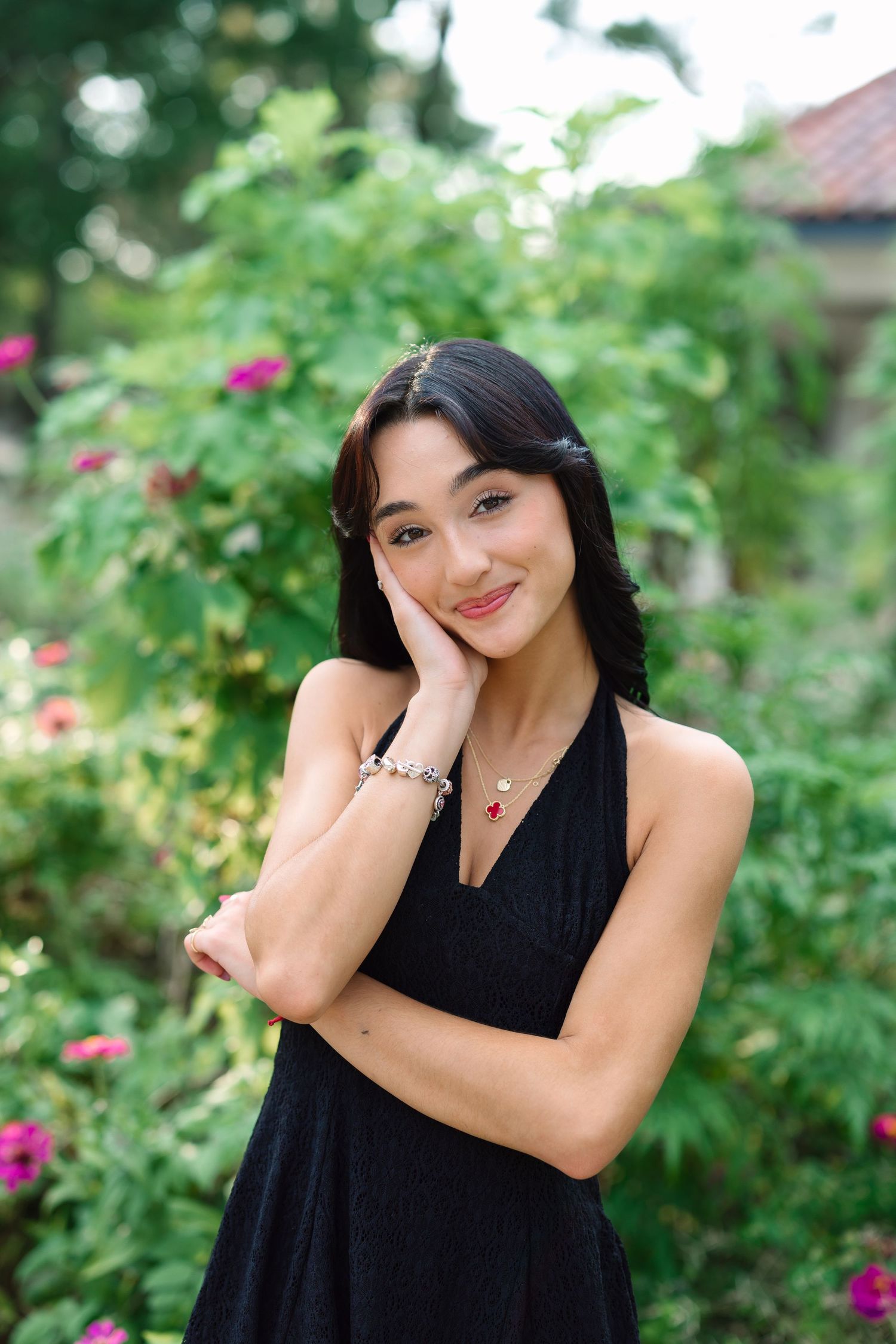 A series of playful poses in a black dress against a garden backdrop with pink flowers.