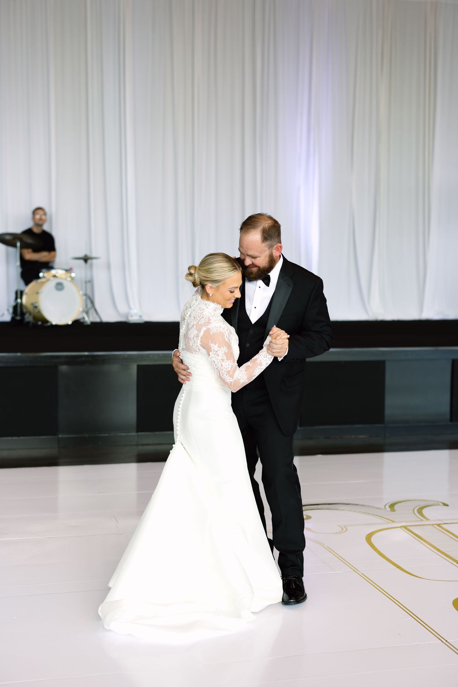 Bride and groom share their first dance, bride in lace mermaid gown, groom in black tuxedo.