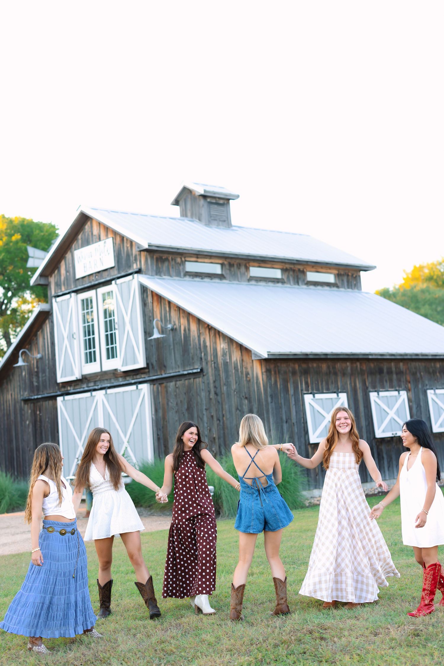 Group dancing and holding hands in front of a weathered barn with white trim.