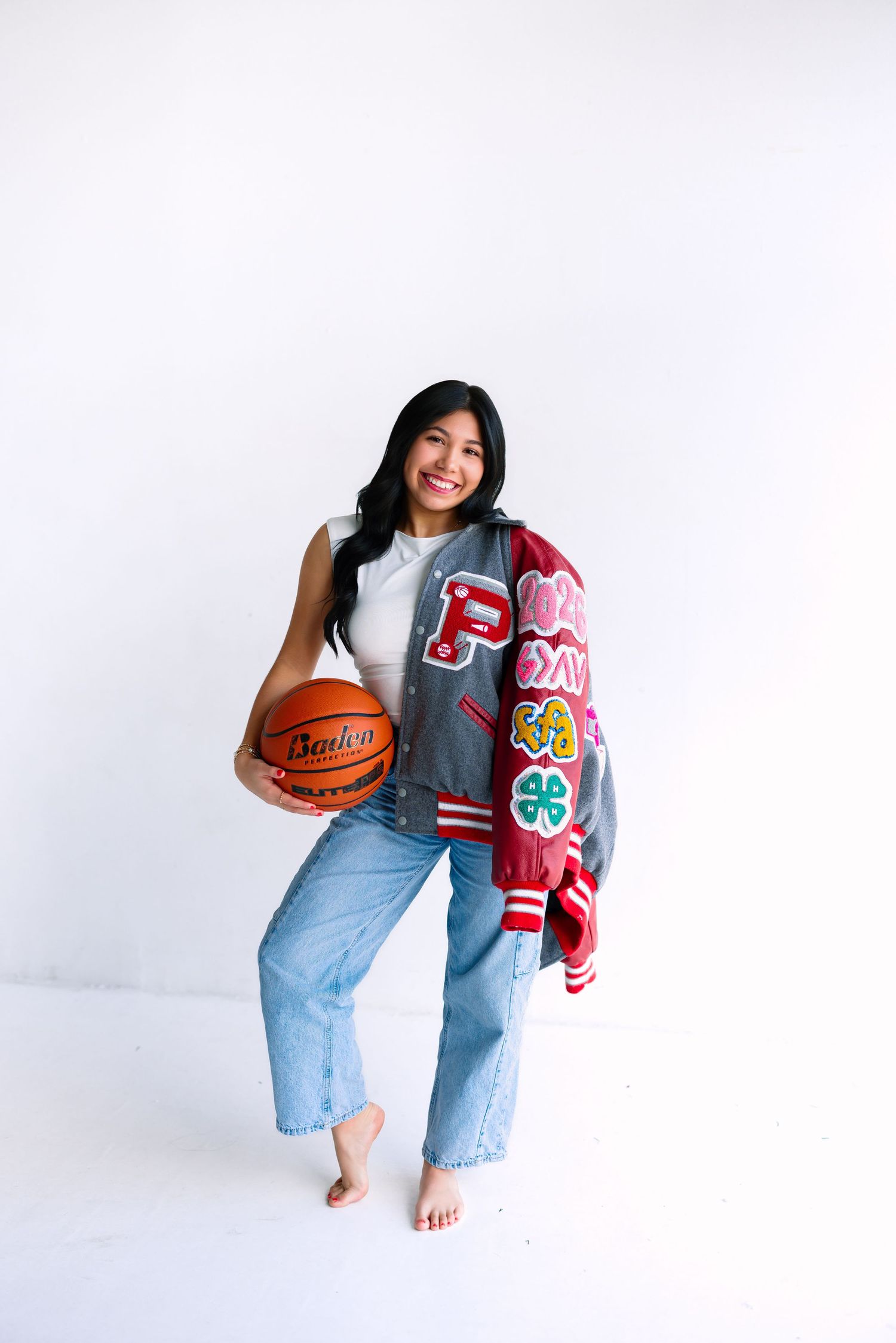 Casual portrait with varsity jacket and basketball against white backdrop.