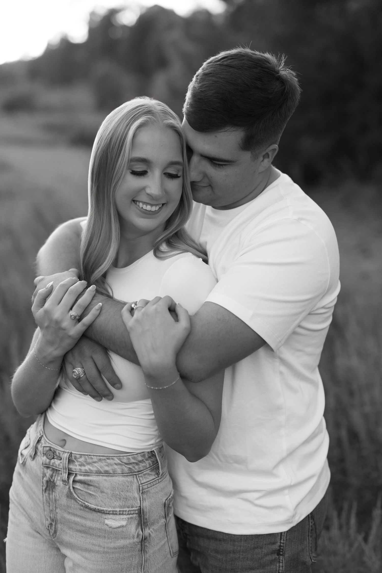 Black and white photo of a smiling couple embracing outdoors, woman in white top and jeans, man in white t-shirt.