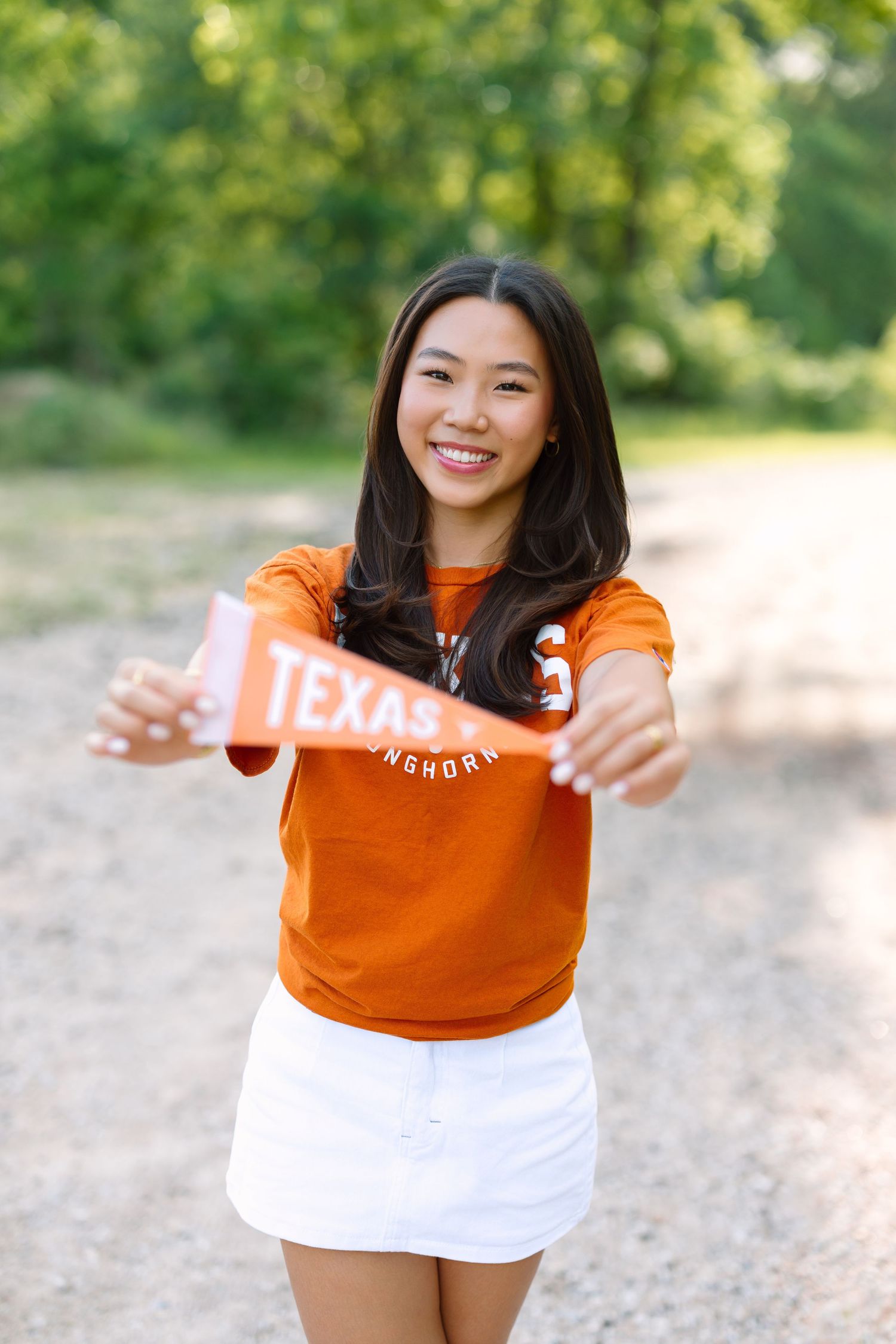 Smiling young woman in orange Texas Longhorns shirt and white skirt holding a pennant outdoors.