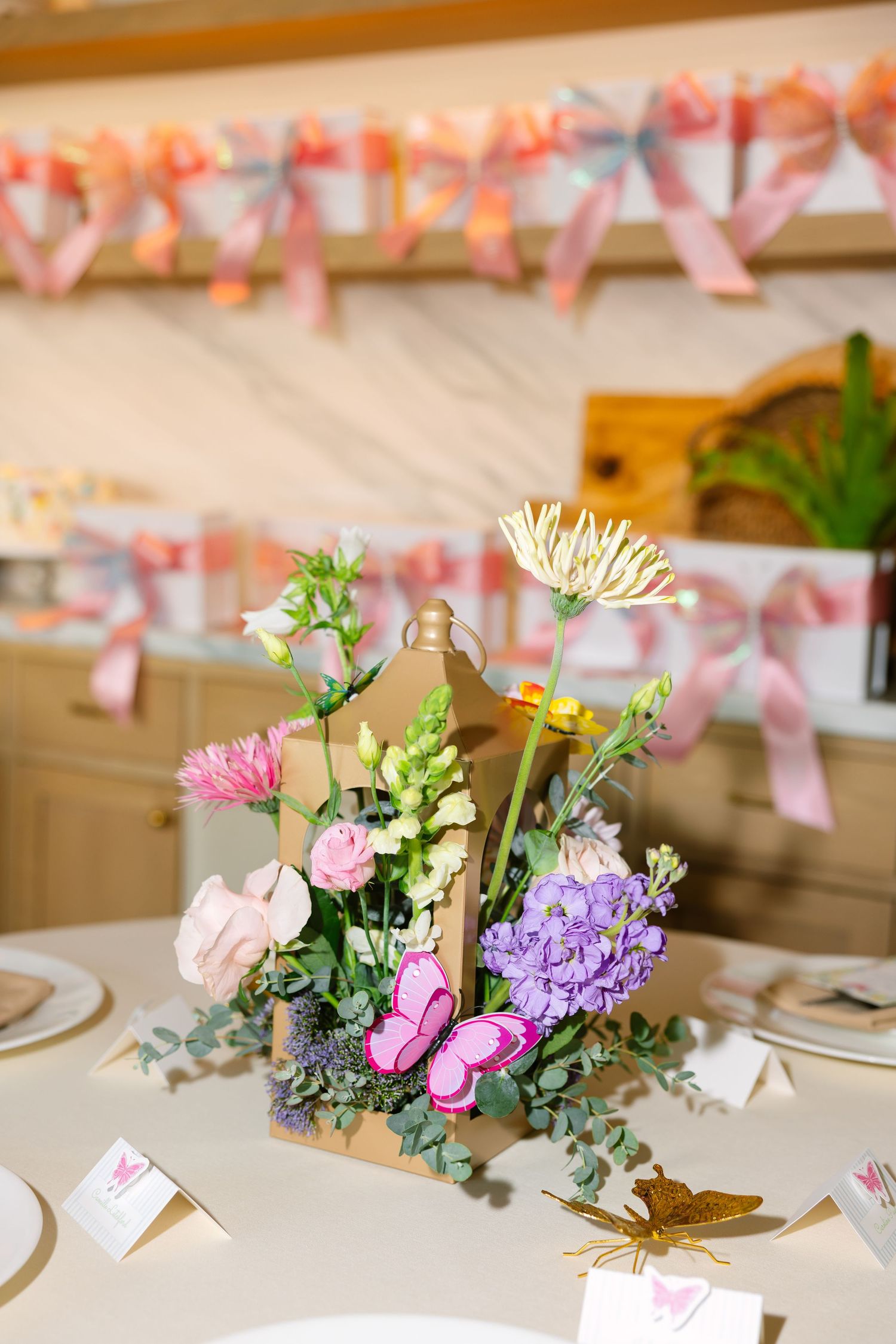 Colorful floral centerpiece with butterflies in a wooden box on a table at a pink-themed party celebration.