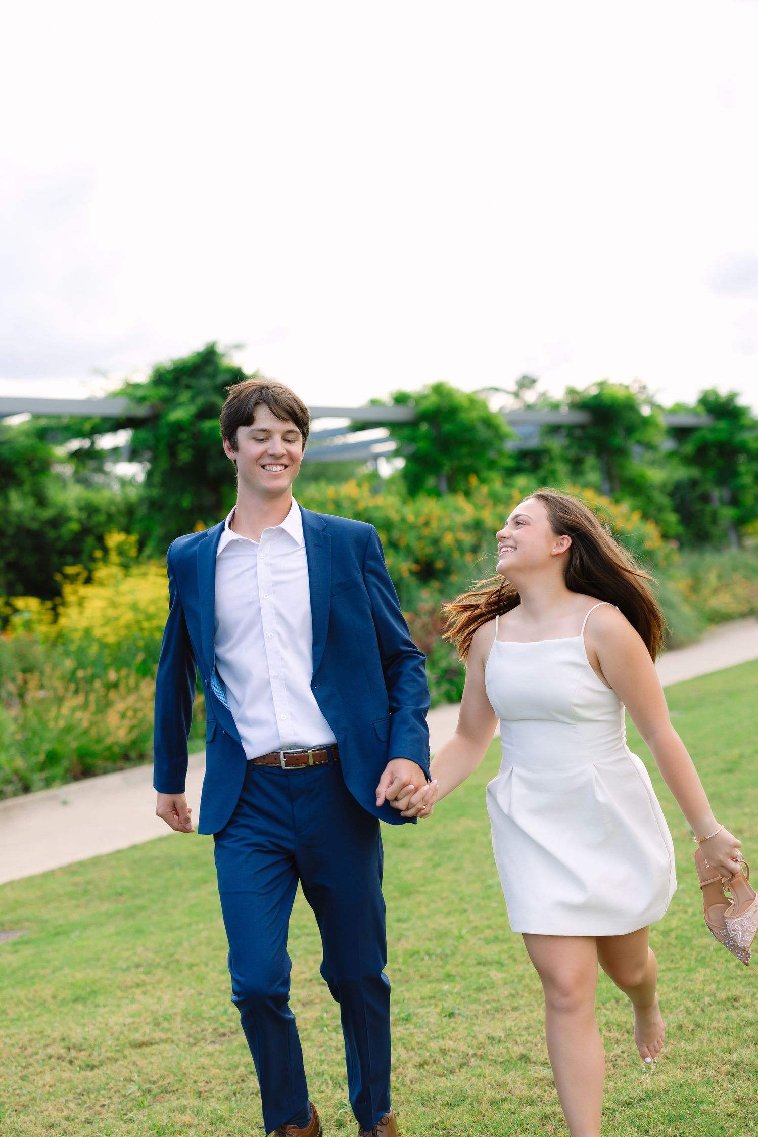 A couple runs playfully through a grassy field on a sunny day.