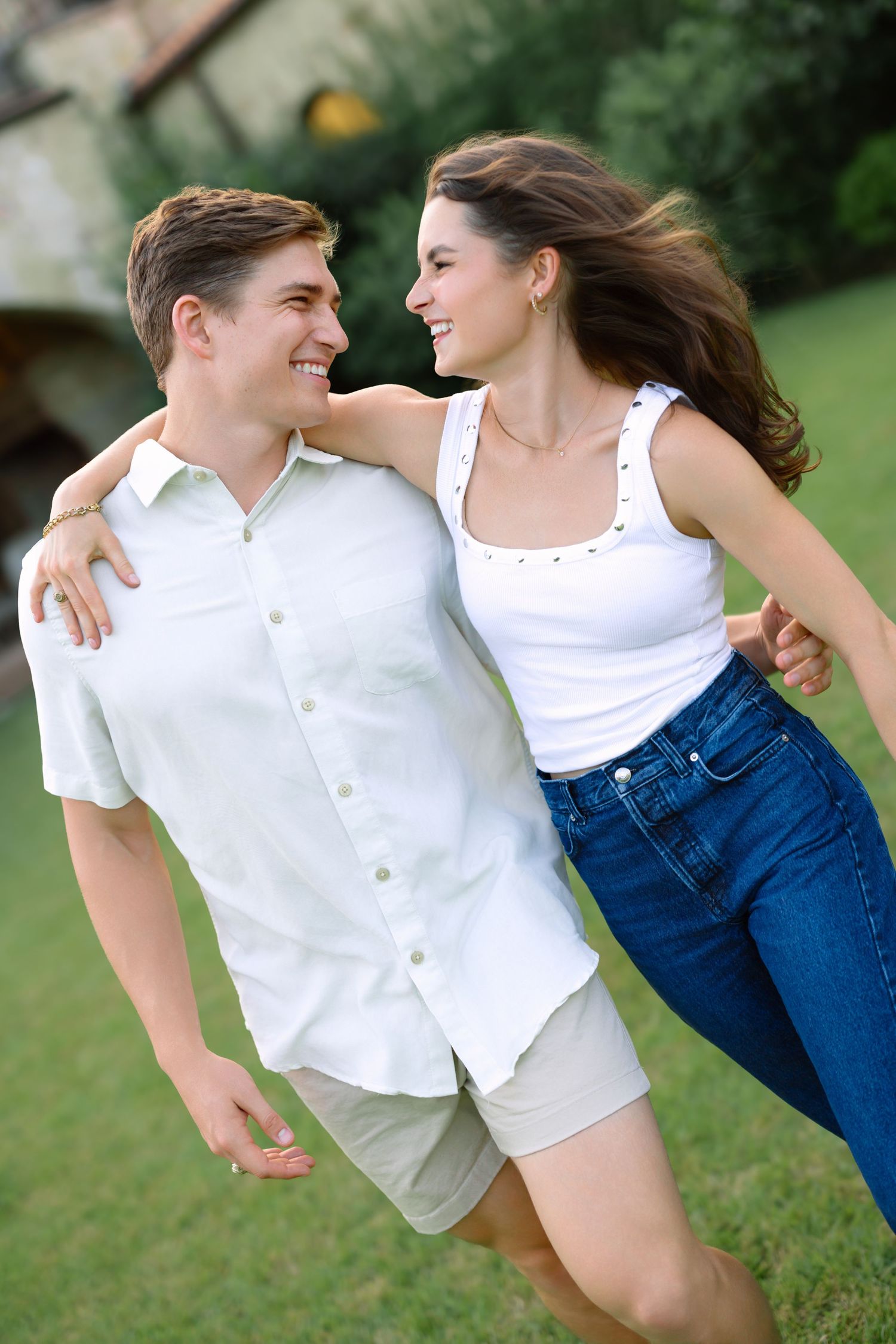 Happy young couple embracing and smiling outdoors, wearing white tops and casual summer clothing in a green yard.