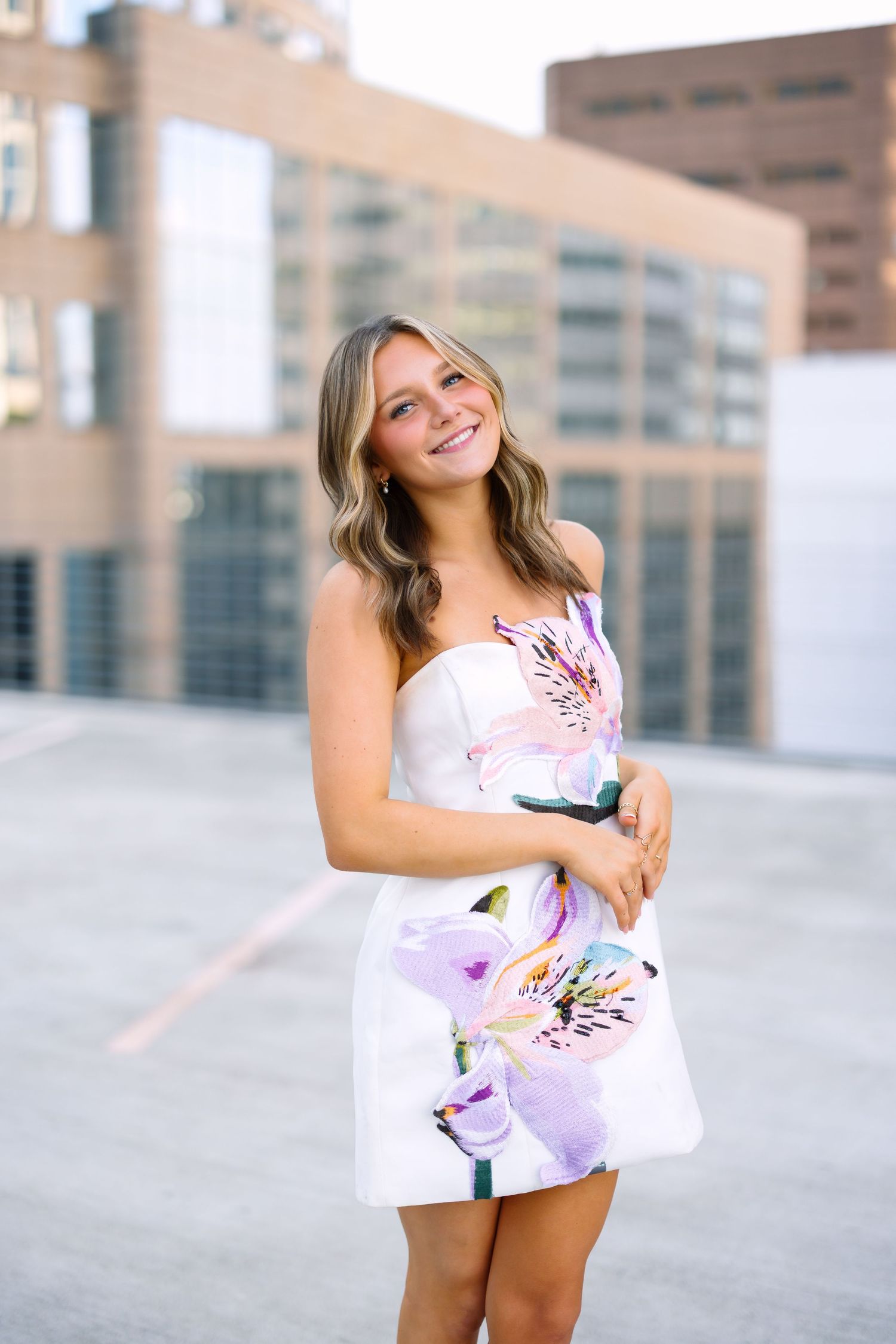 Model in white summer outfit poses against urban building backdrop.