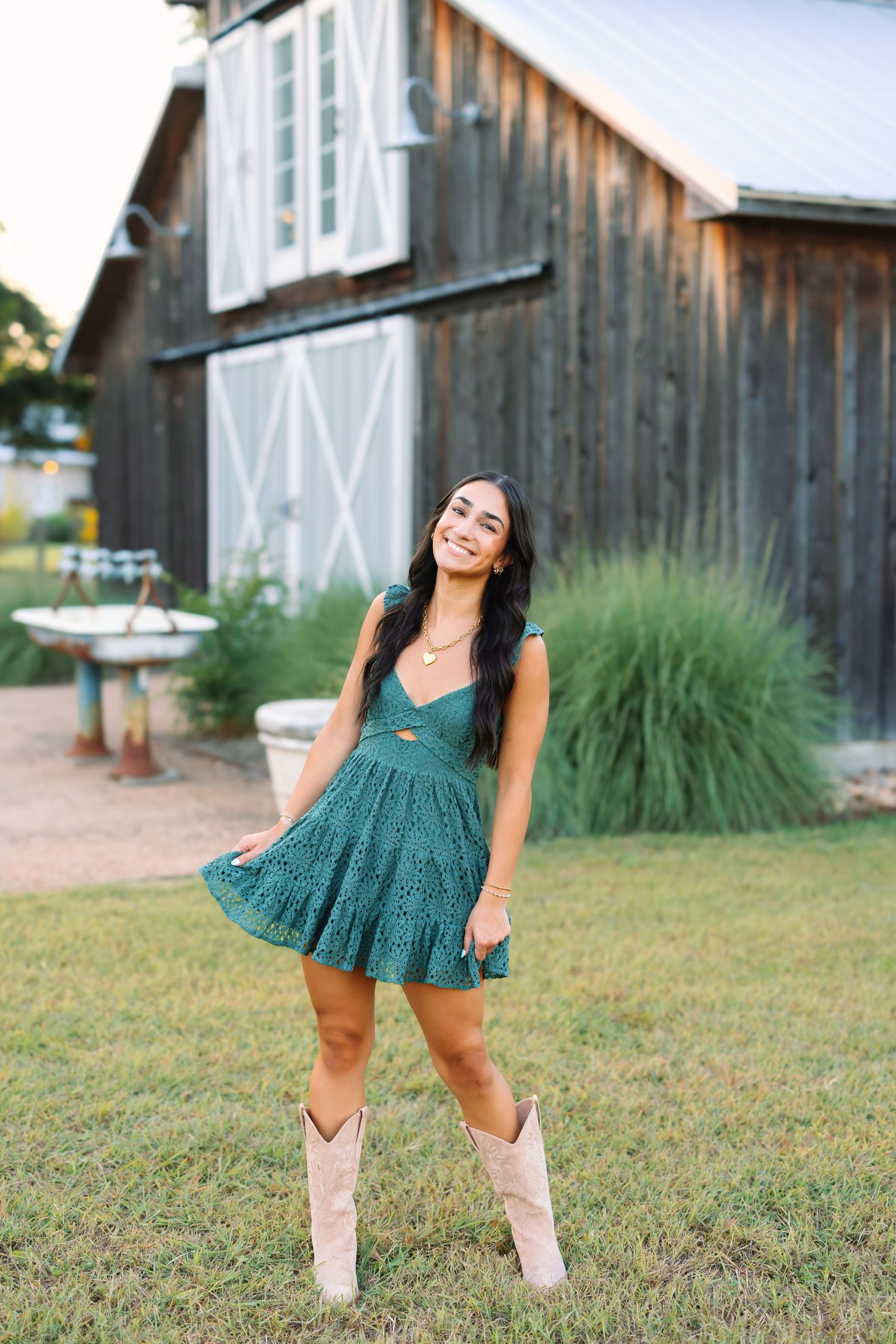 Dynamic poses in a green dress against a rustic barn backdrop with tall grass.