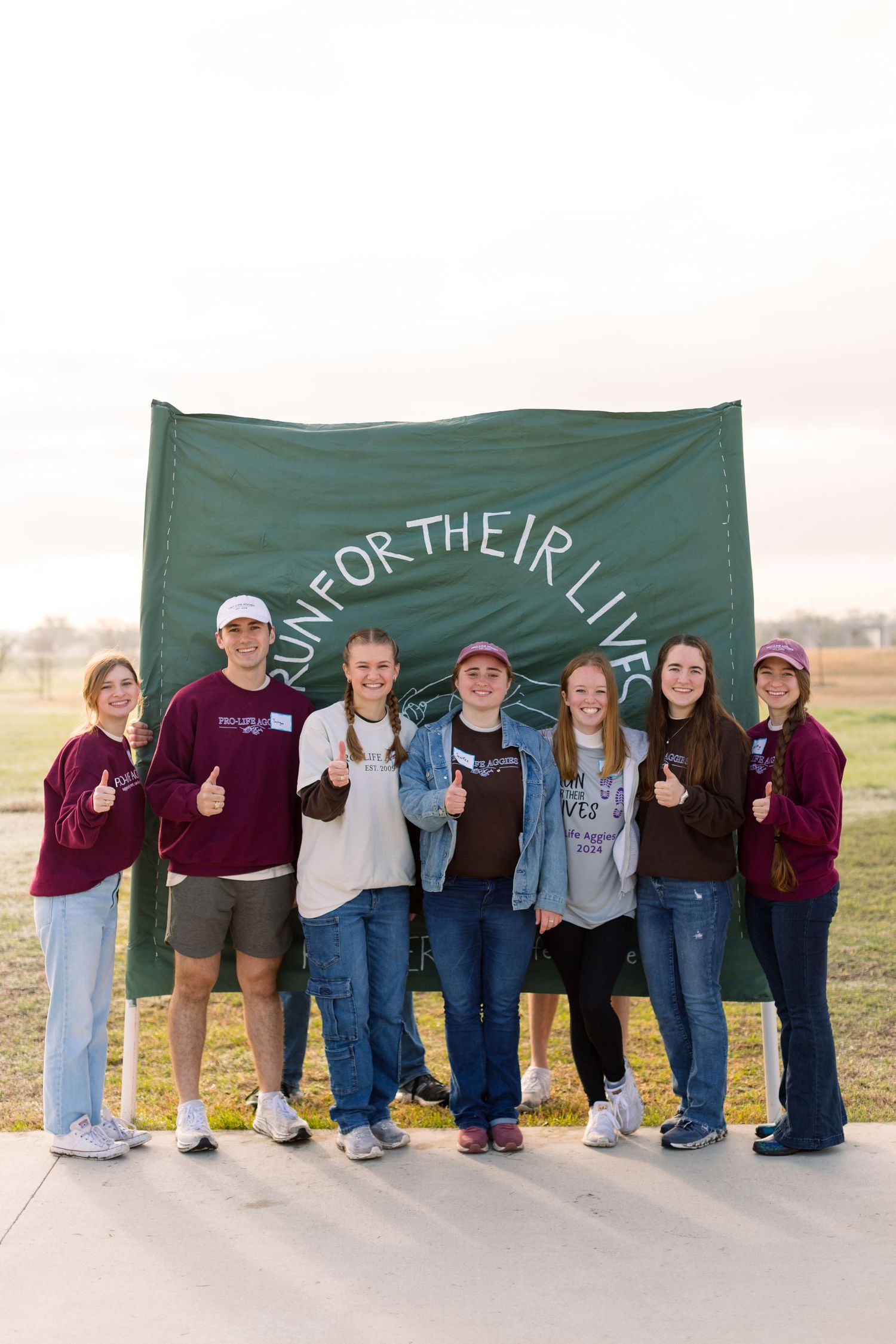 Line of people standing together against a green banner backdrop outdoors.