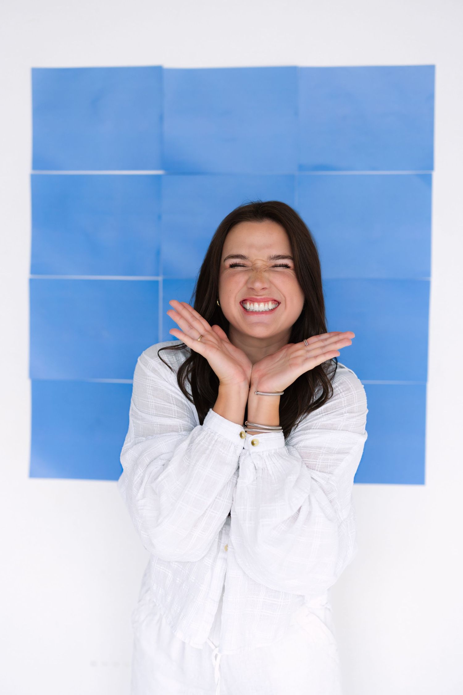 Person in white shirt poses expressively against blue geometric background.