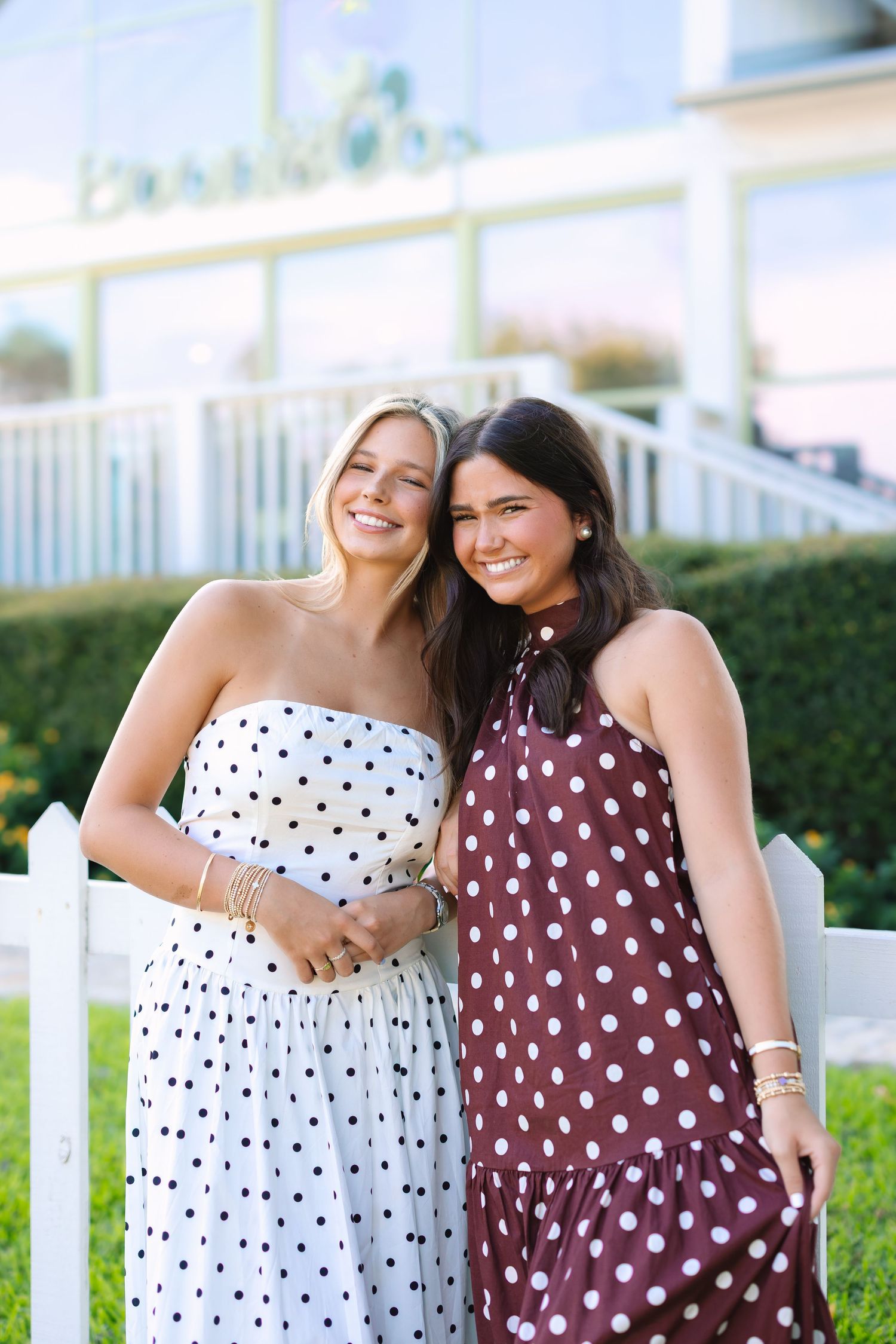 Two friends in polka dot dresses share a joyful moment outdoors.