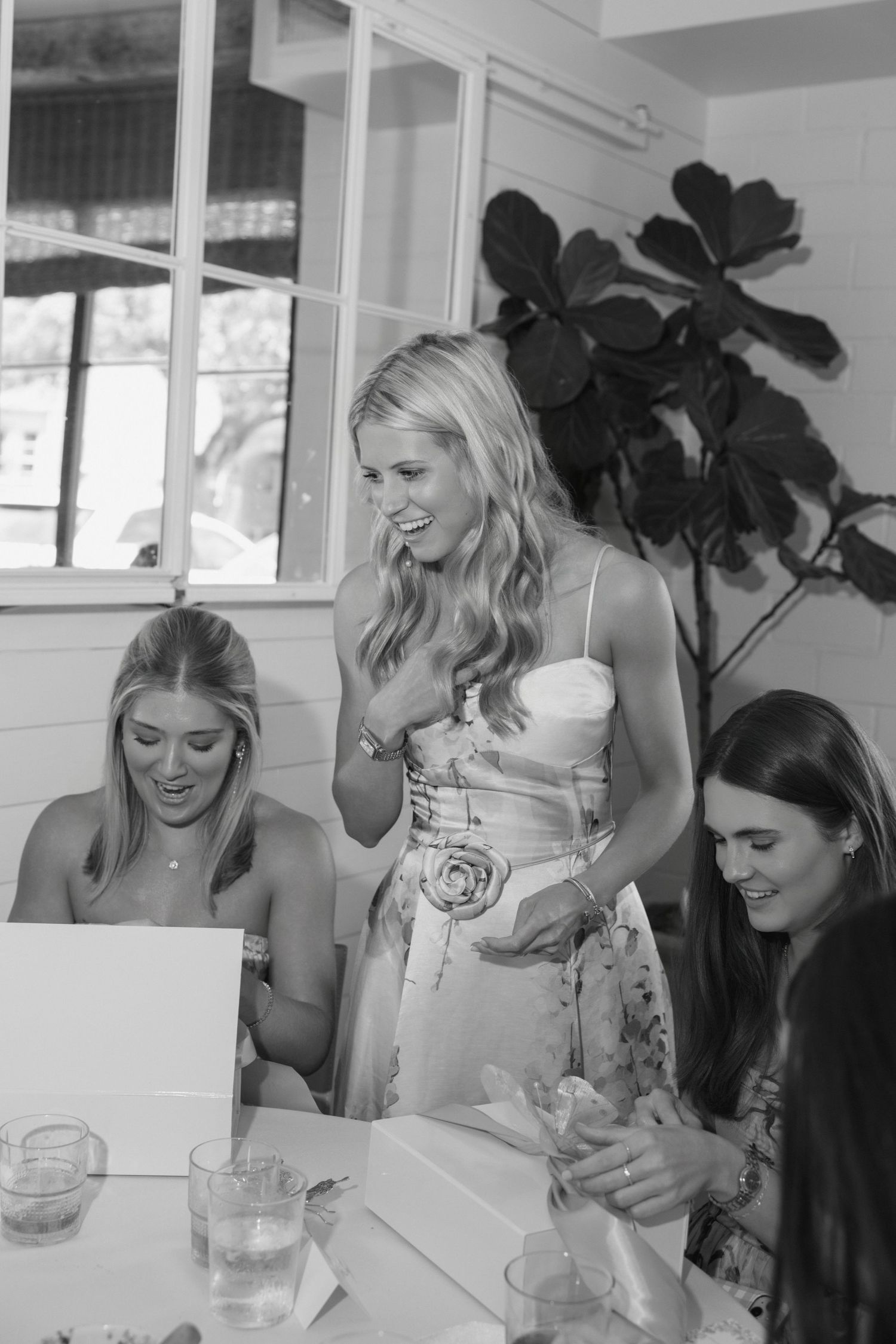 Three women smiling and laughing together at a table during a celebration, black and white photo.