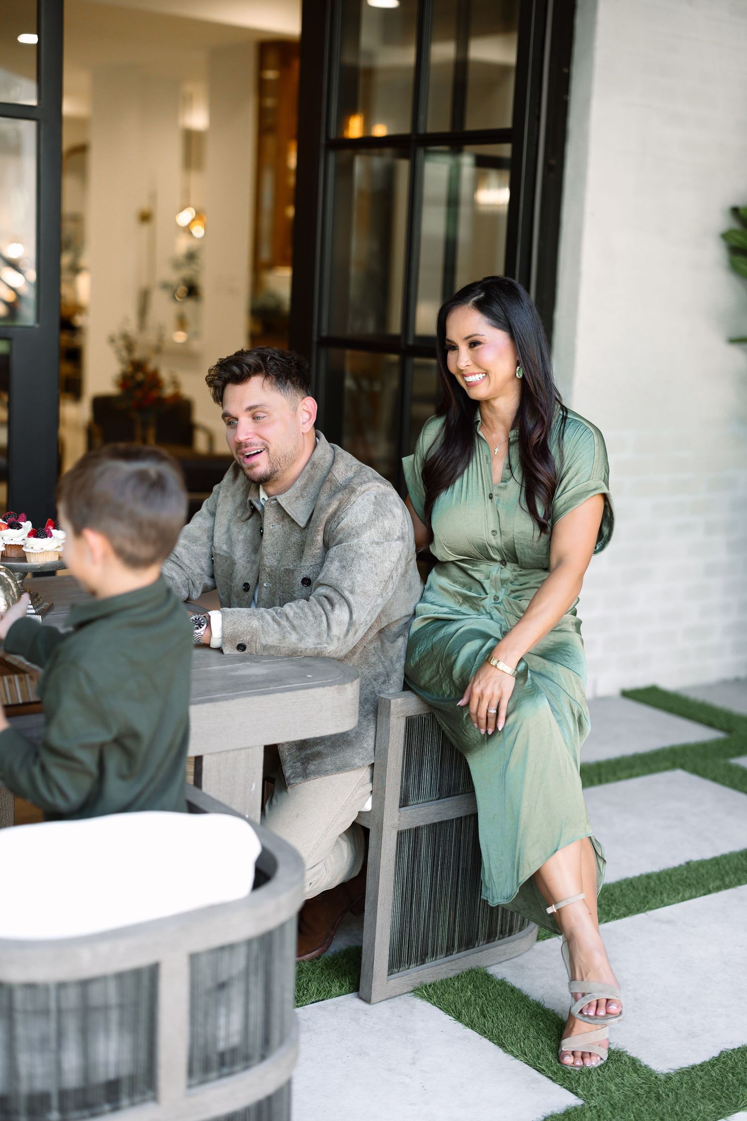 A smiling family in green outfits relaxing at an outdoor patio table, enjoying a casual gathering together.