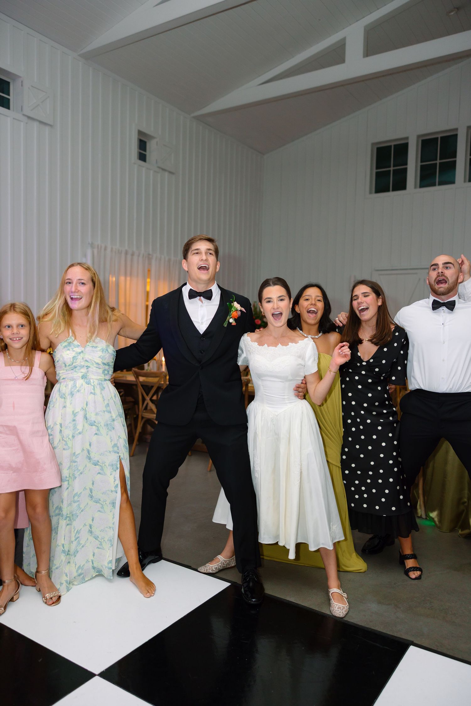 Bride and groom celebrating joyfully with wedding guests on a checkered dance floor at reception.