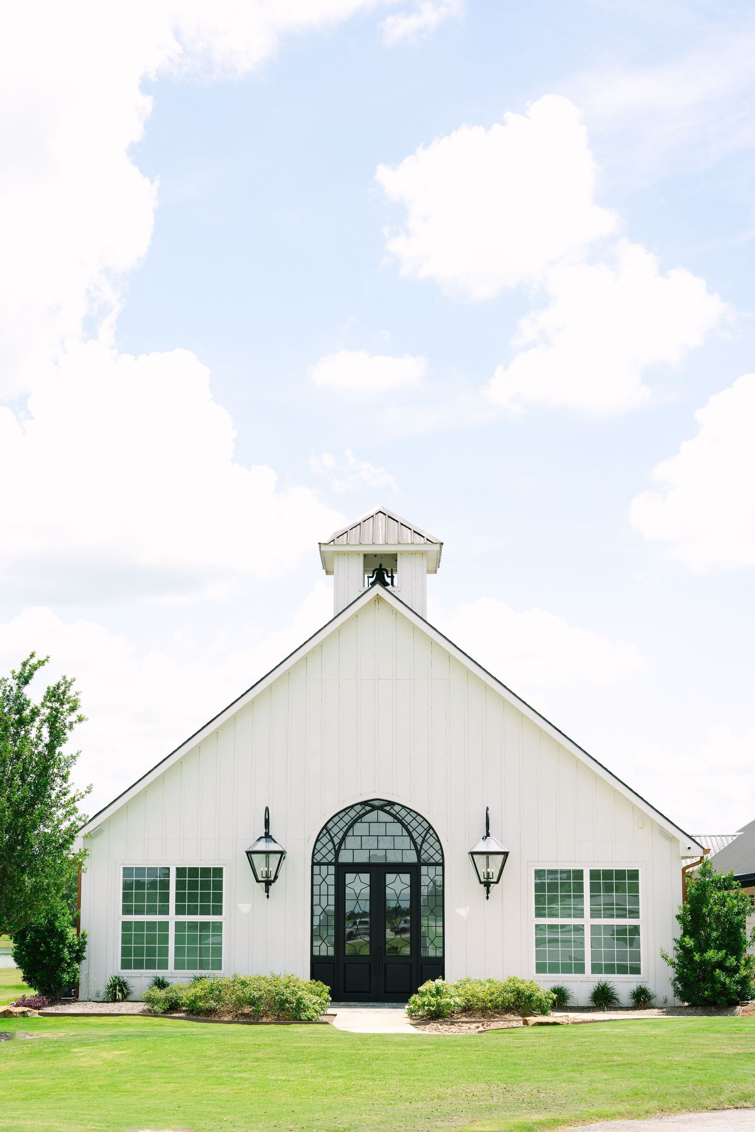 White modern chapel building with symmetrical design featuring black arched windows and exterior lighting.
