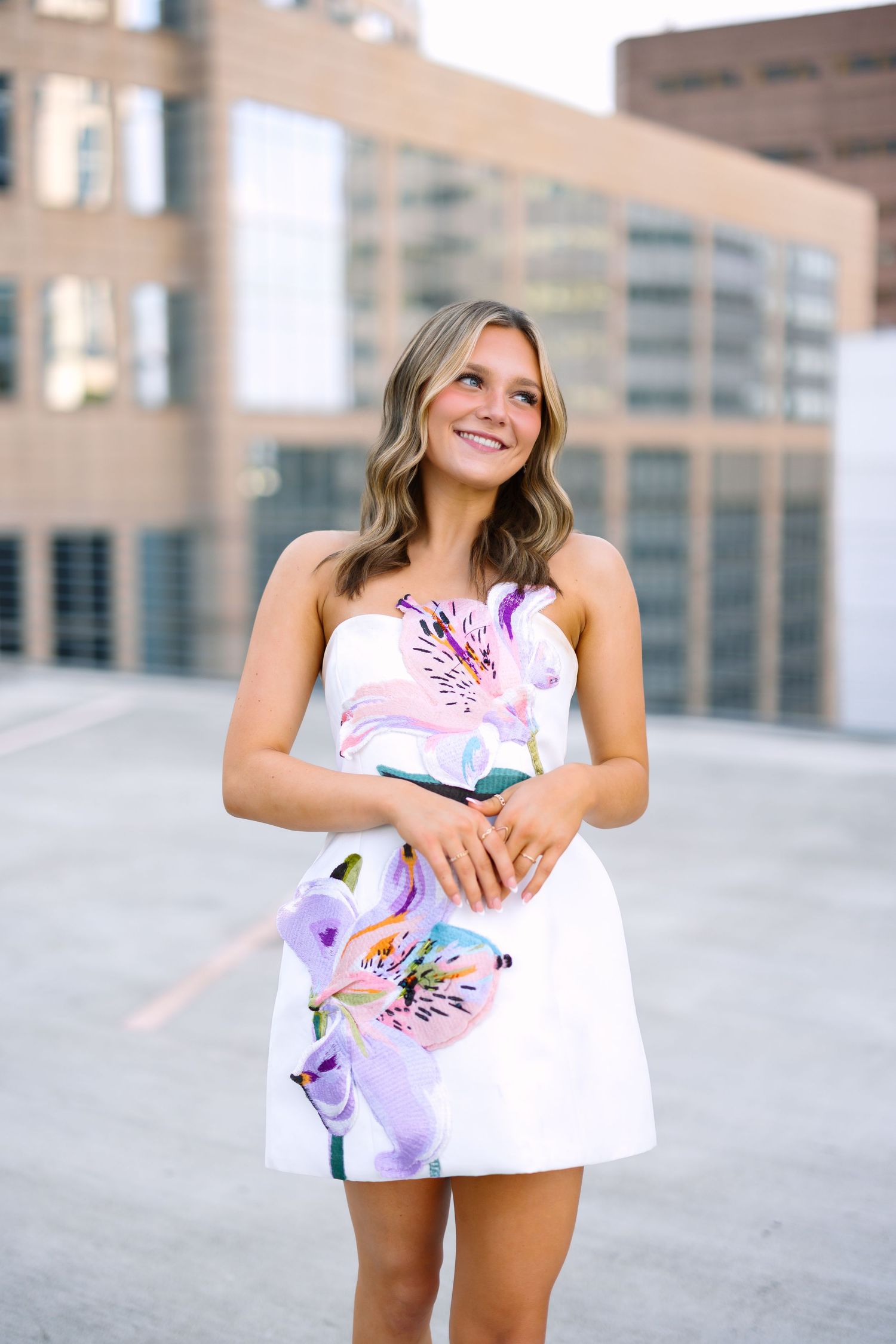 A collage of four photos showing someone in a white and floral print dress posing against an urban backdrop.