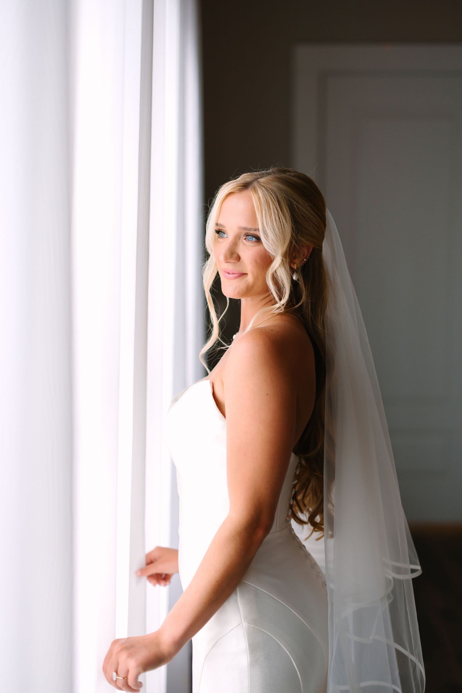Soft window light illuminates a bride in her wedding gown.