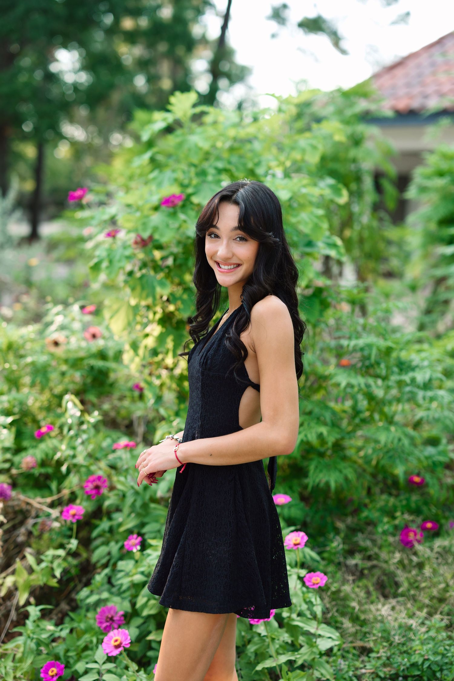 Candid shots in a black summer dress surrounded by lush greenery and pink blooms.