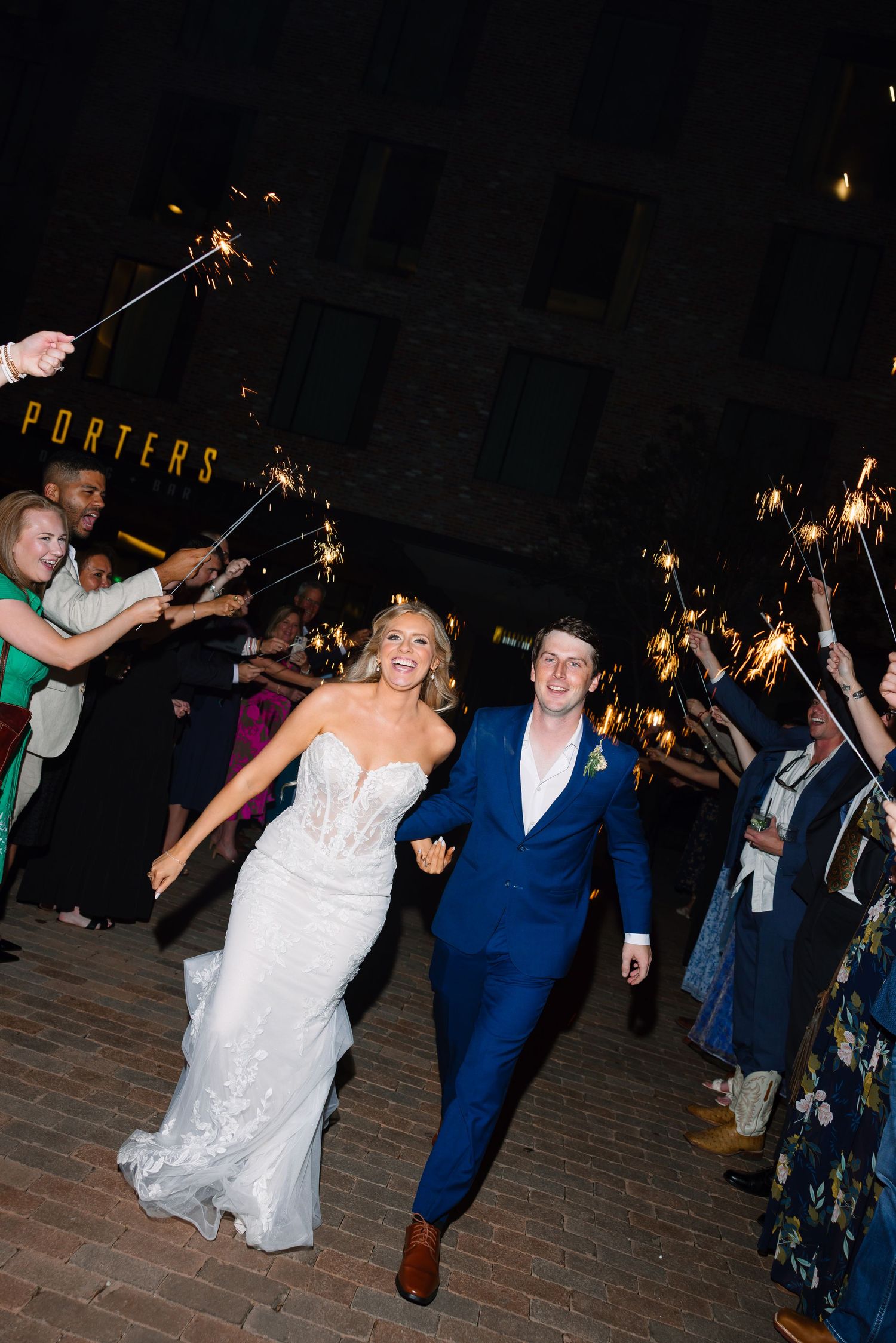 Newlyweds run through sparkler exit tunnel outside Porters venue at night wedding celebration.