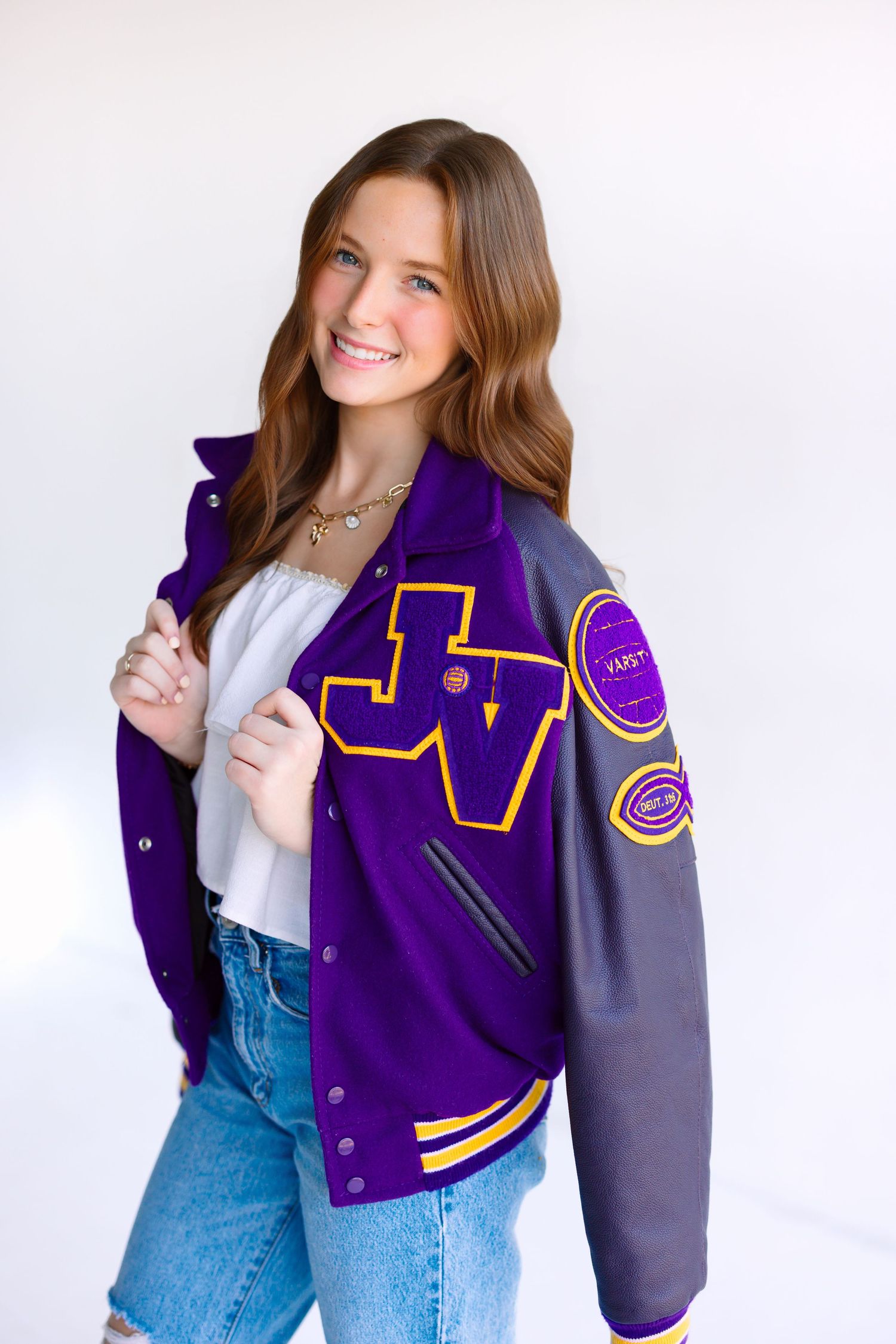 Lifestyle portrait wearing purple and gray varsity letterman jacket with white top and jeans.