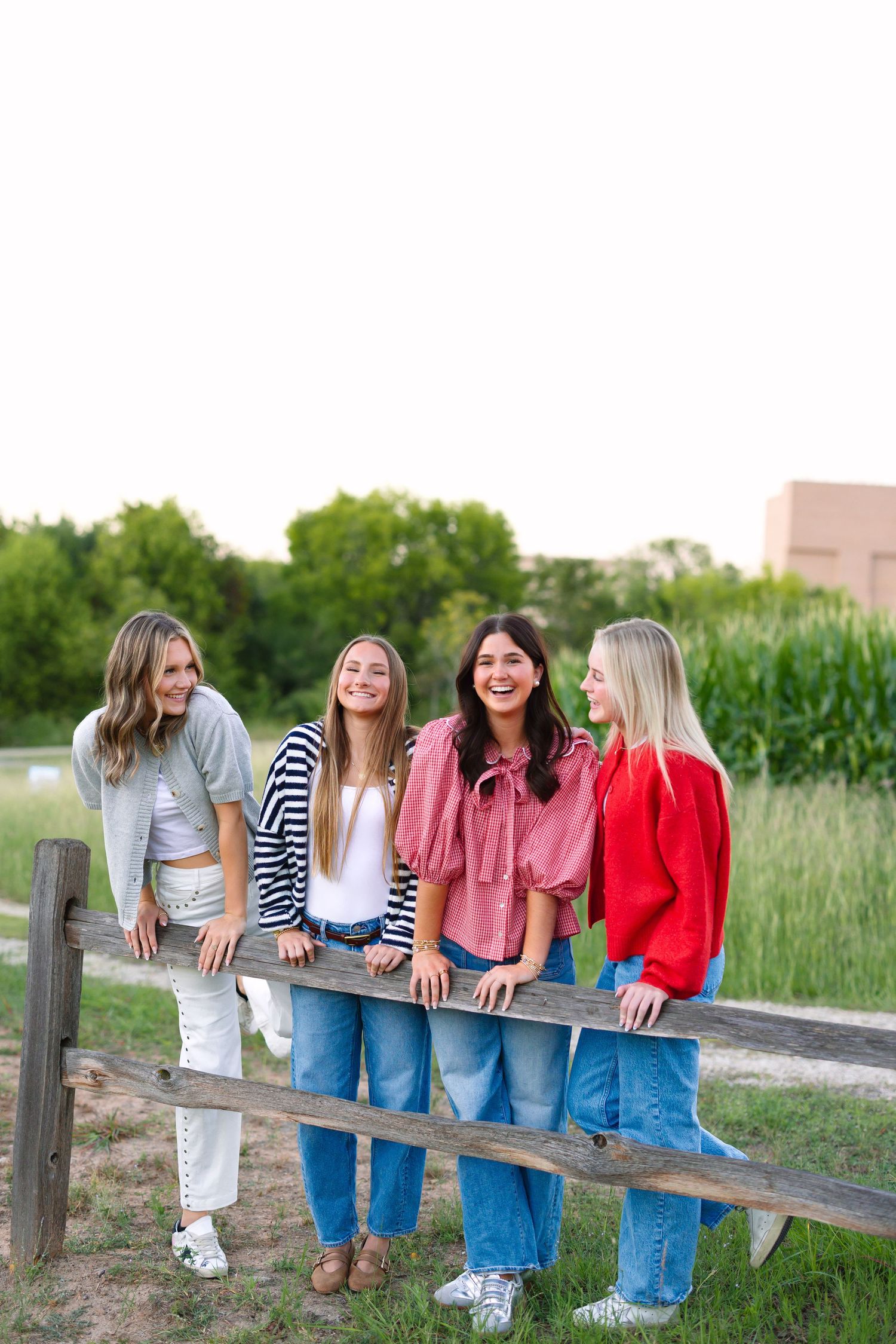 Friends sitting on wooden fence laughing together in casual outfits during golden hour.